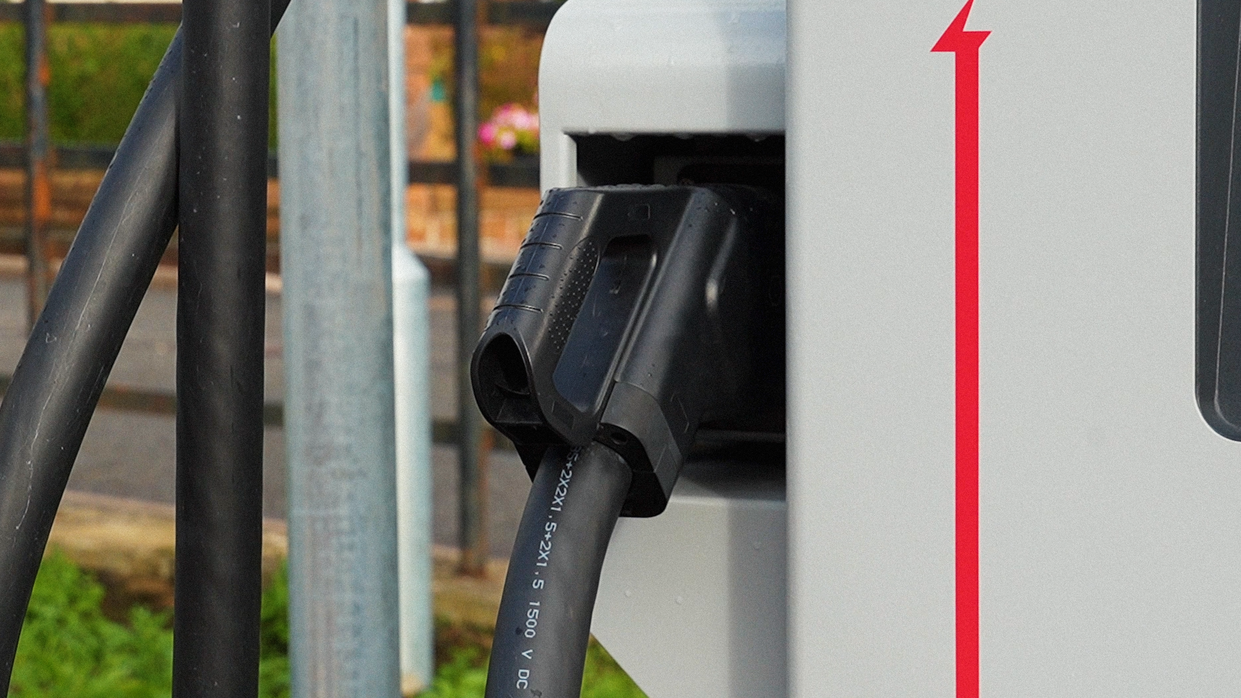 Close-up of an electric vehicle charging station with two black charging cables plugged in, and a red arrow indicating the charging process.