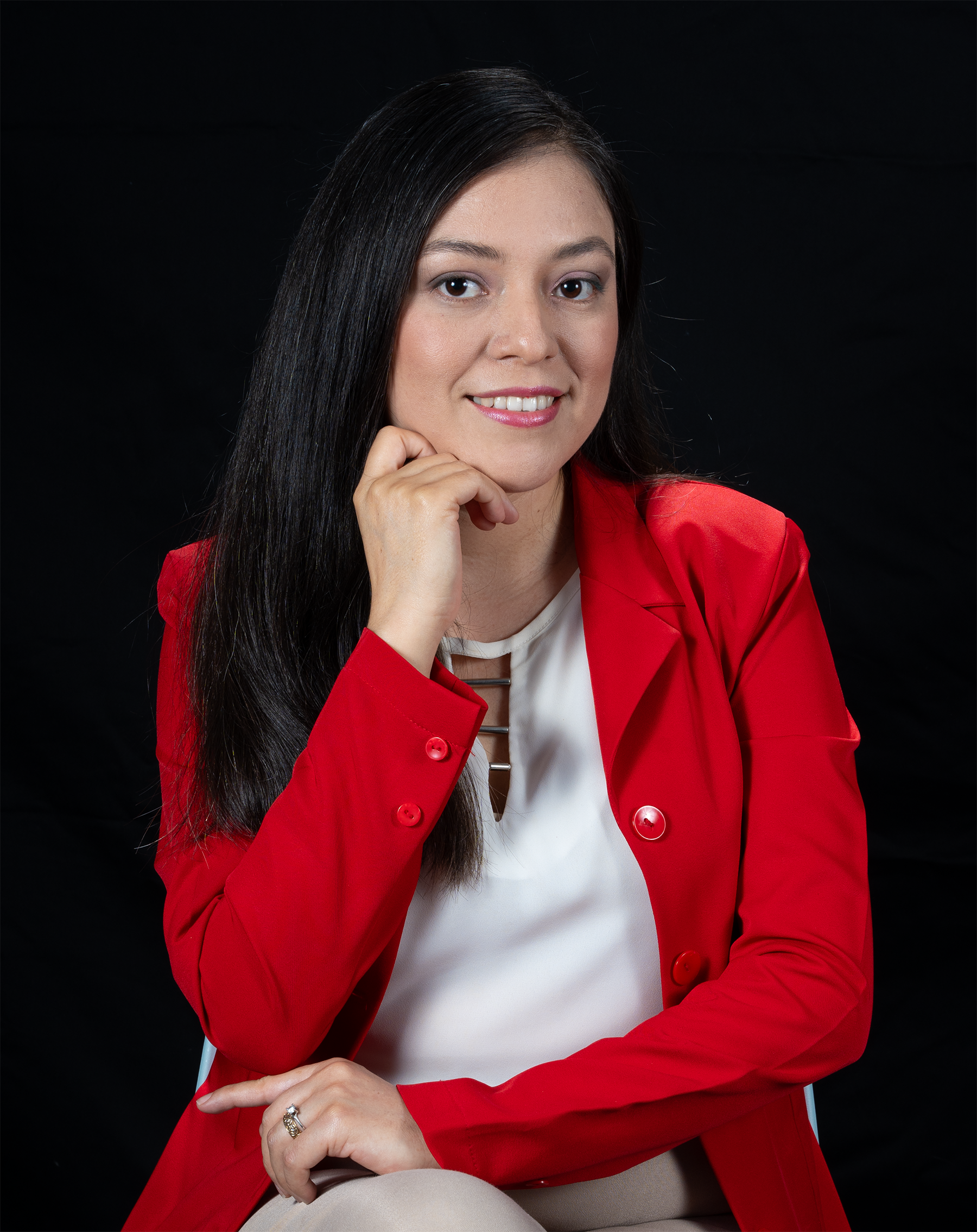 Retrato de una mujer de cabello largo y oscuro, con una sonrisa y usando blusa blanca y chaqueta roja, sentada contra fondo negro.