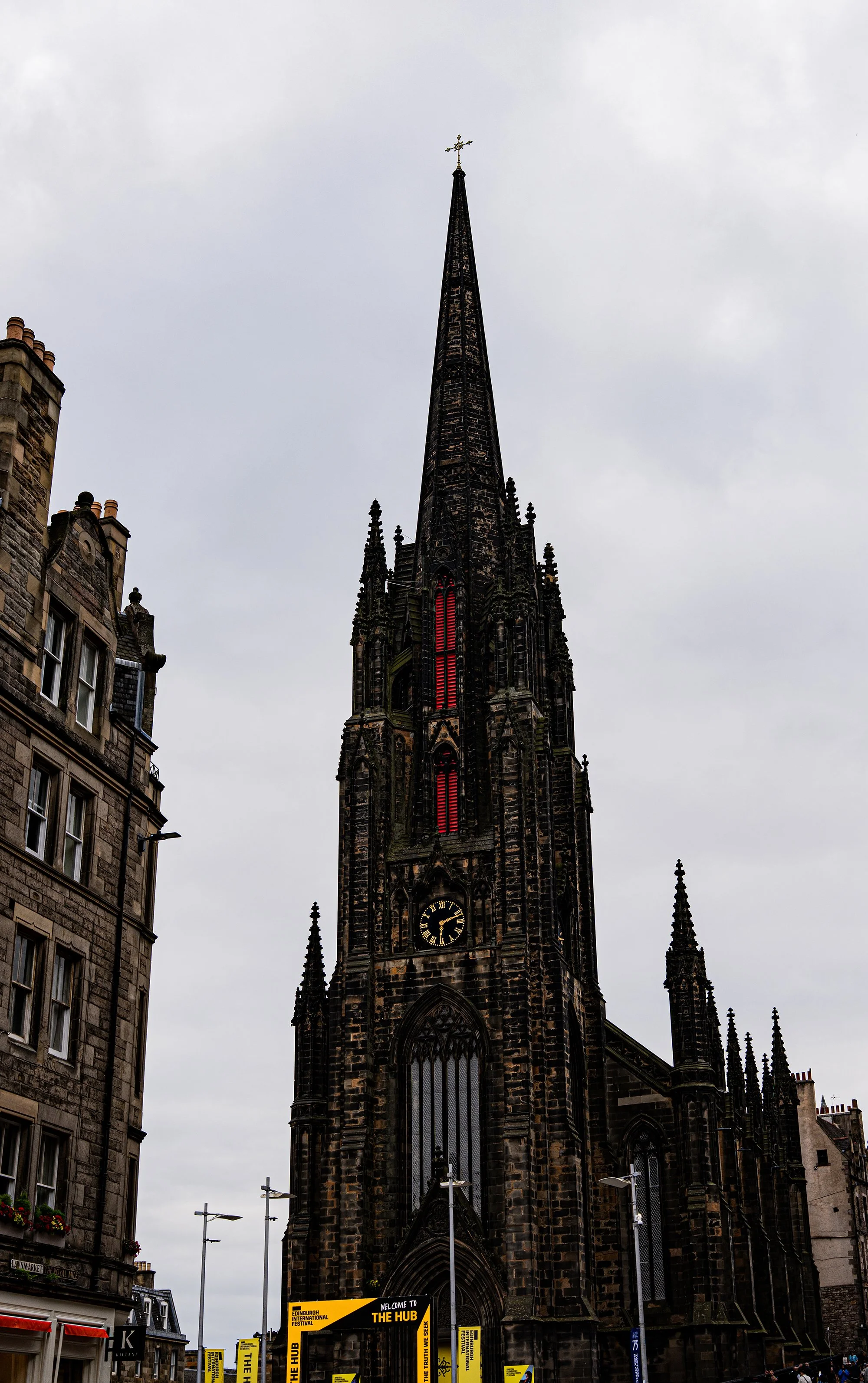 Iglesia gótica con reloj en la fachada, rodeada de edificios y bandera de festival en primer plano