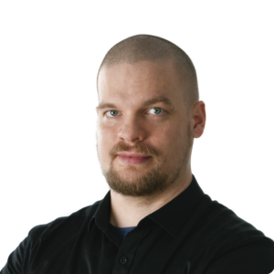 Valokuva nuoresta miehestä, jolla on lyhyet hiukset ja parta, hän katsoo kameraan ja on pukeutunut mustaan paitaan.