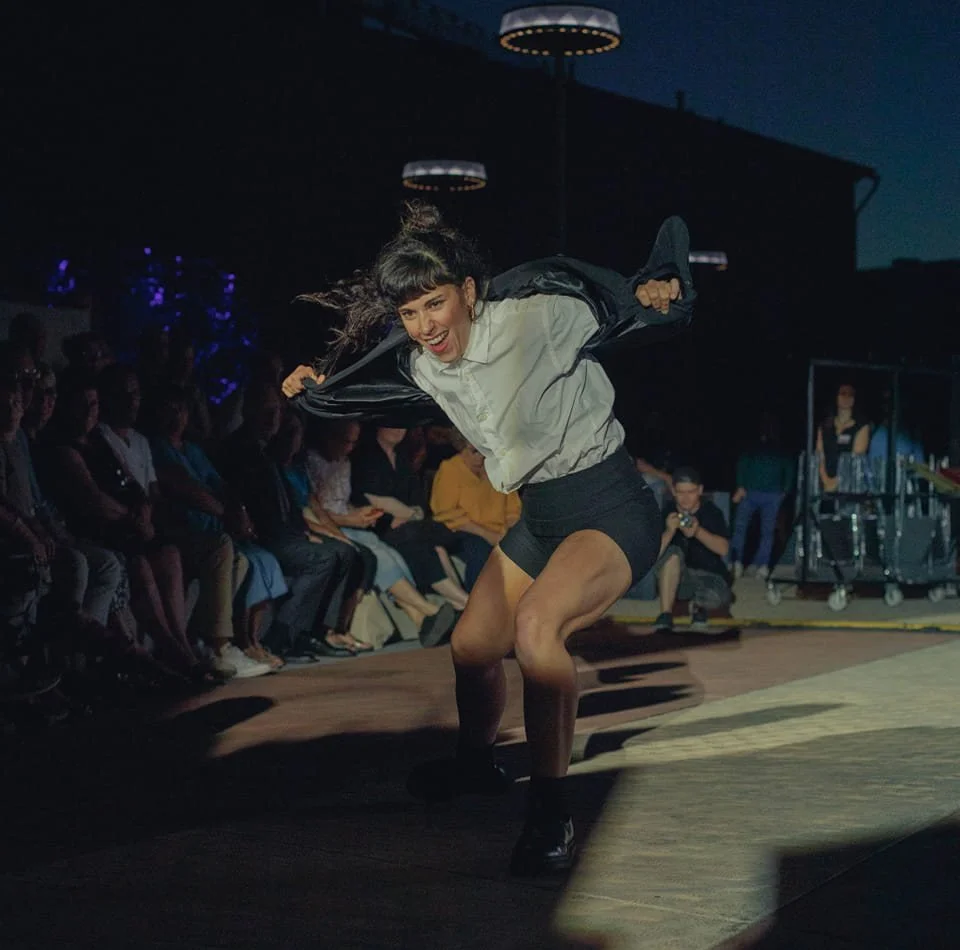 Une femme danse dans un spectacle en plein air lors de la nuit, entourée par un public assis.
