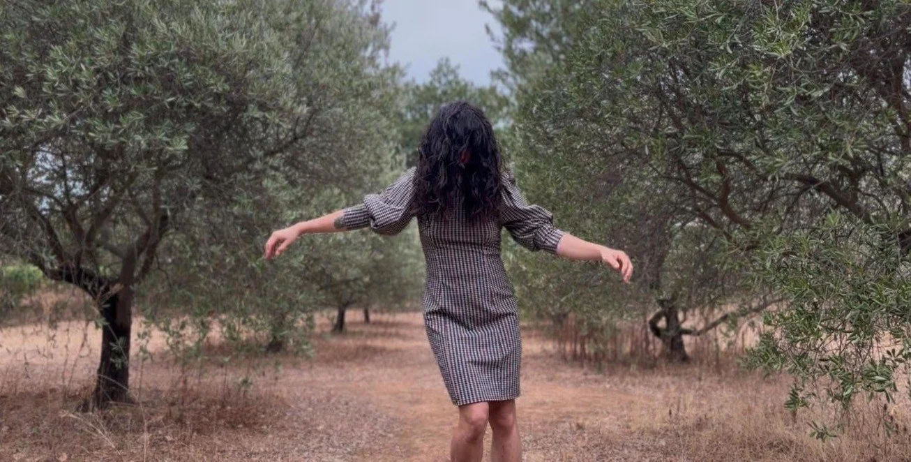 Femme marchant dans une forêt d'arbres avec des branches vertes et un sol de terre.