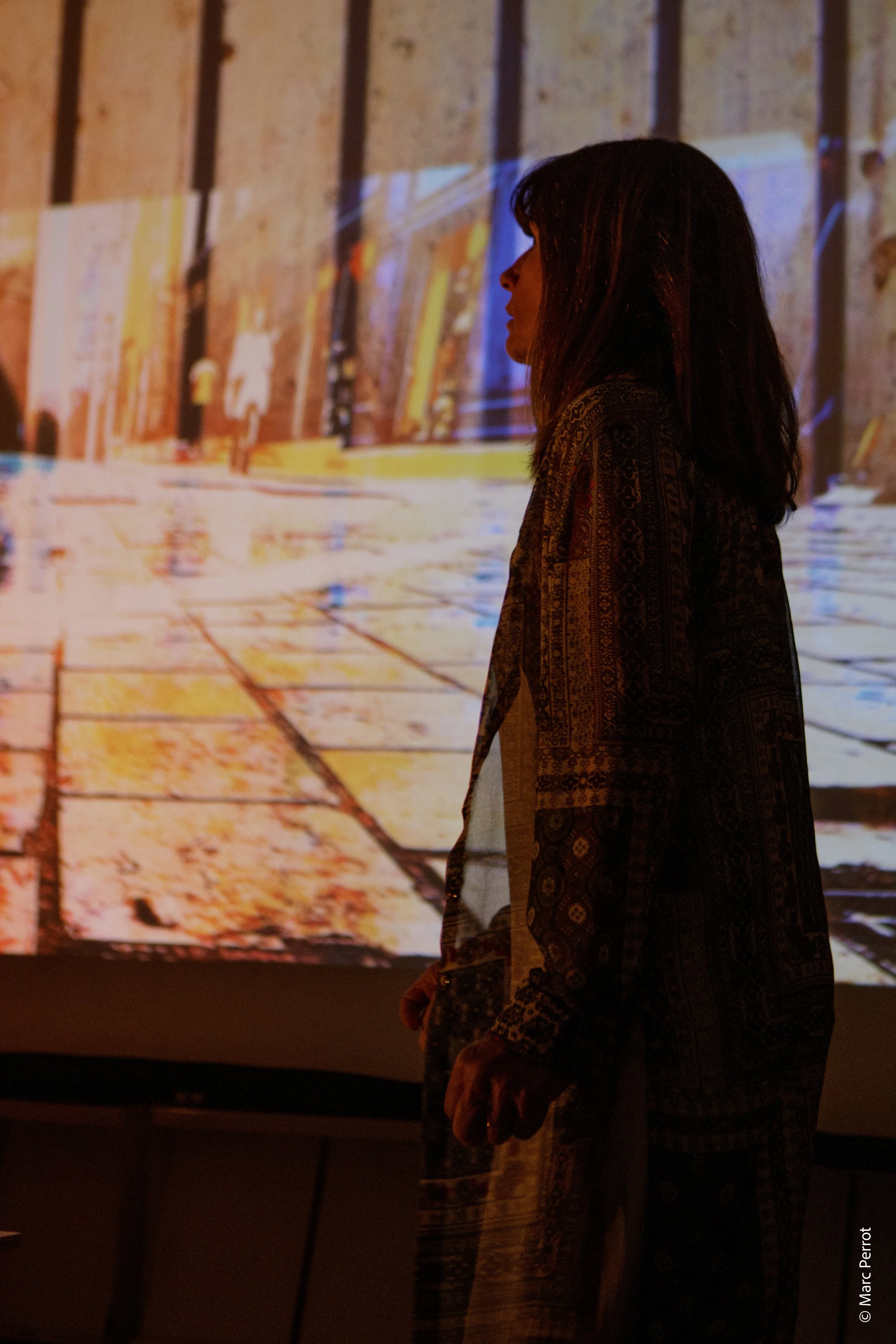 Une femme regarde une projection d'une image de ville ou de bâtiment dans un environnement sombre.