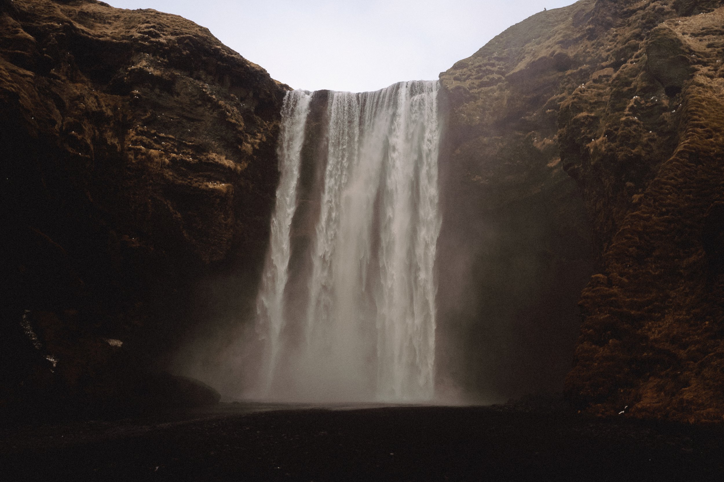 A waterfall cascading down from cliffs into a pool below surrounded by rocky terrain.