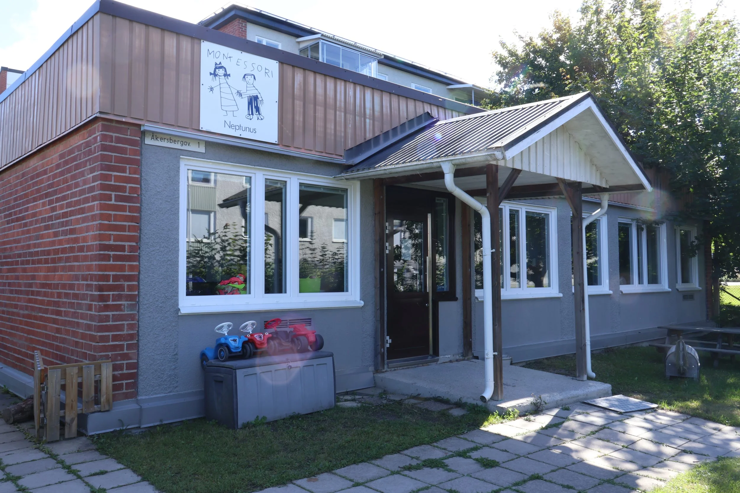 Framsida av ett hus med en skylt som visar en ritning av två leksaksfigurer och texten 'Montessori Neptunus'.