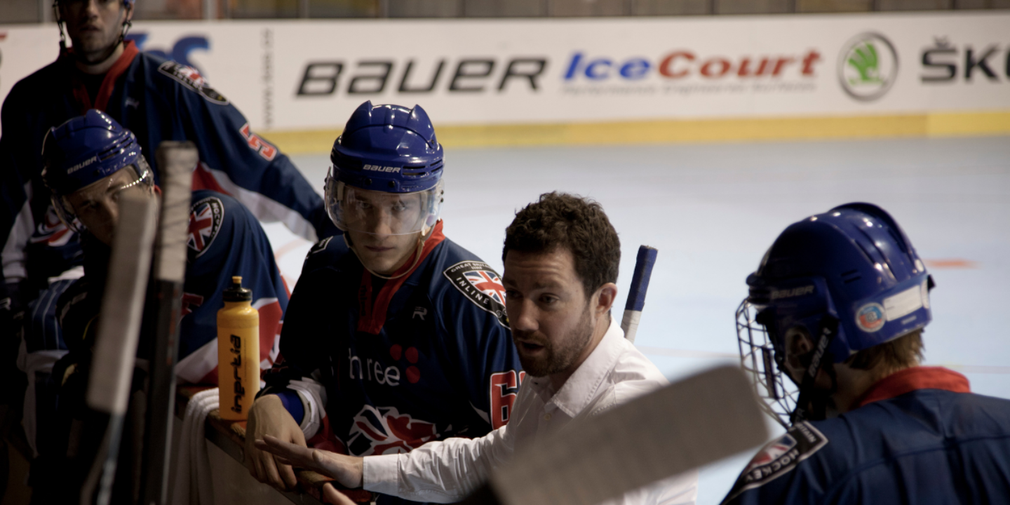 Andrew Sillitoe on the bench during a game or practice, with team jerseys and helmets.