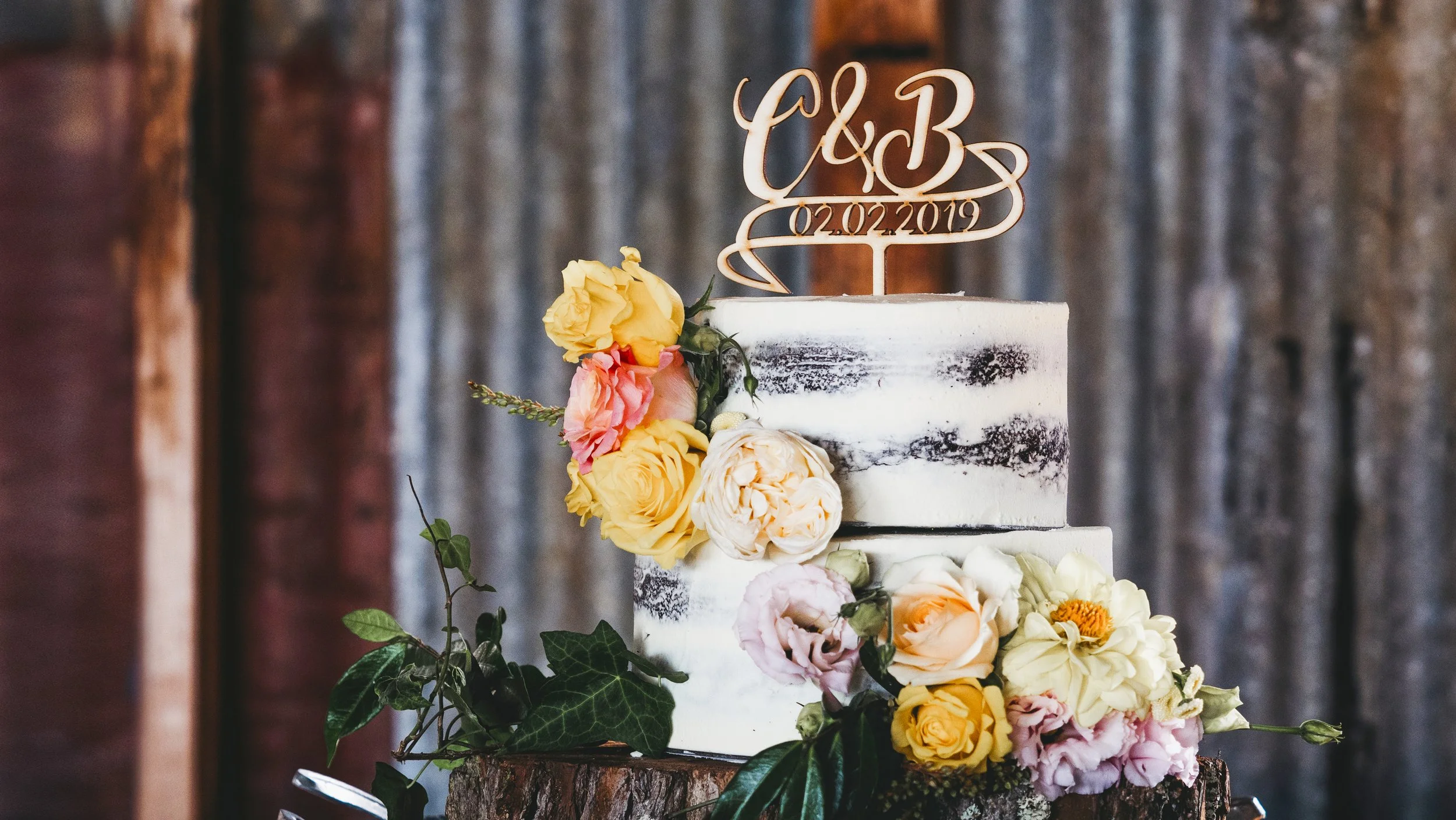 A wedding cake decorated with flowers and a topper that reads 'C & B' with a date '02.02.2019'