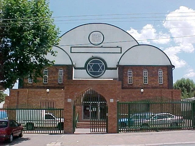 Building with a synagogue windows and Star of David symbol above the entrance, surrounded by a metal fence.