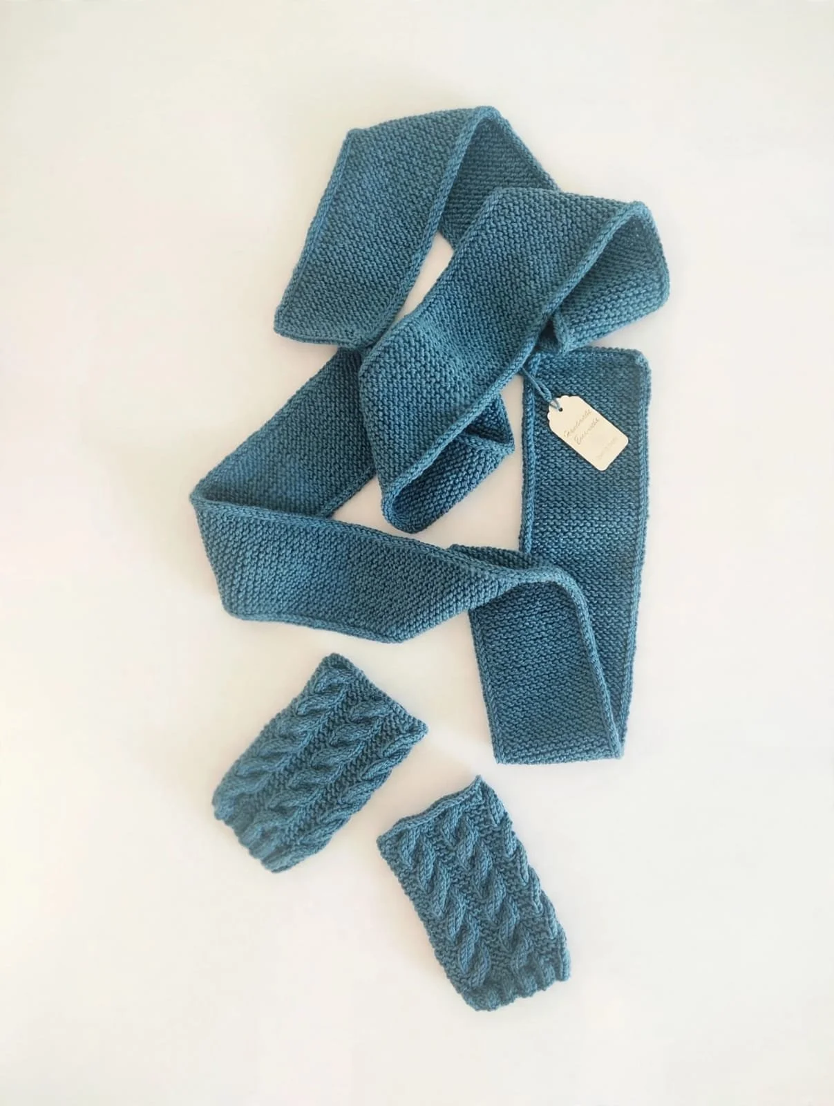 Sciarpa sottile in maglia color petrolio distesa con due manicotti a trecce coordinati e cartellino