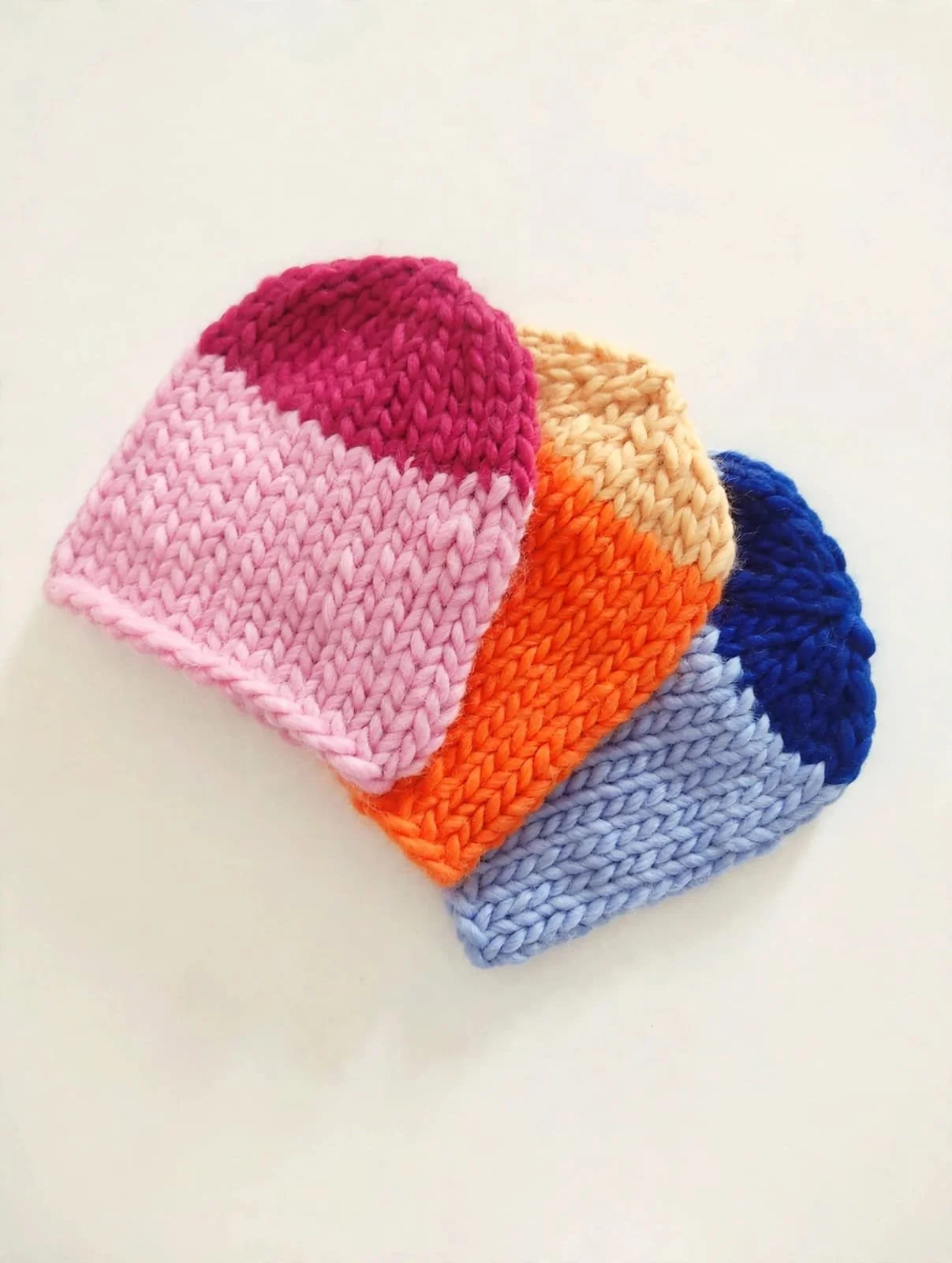 Tre cappelli in lana grossa bicolore sovrapposti, rosa e fucsia, pesca e arancione, azzurro e blu