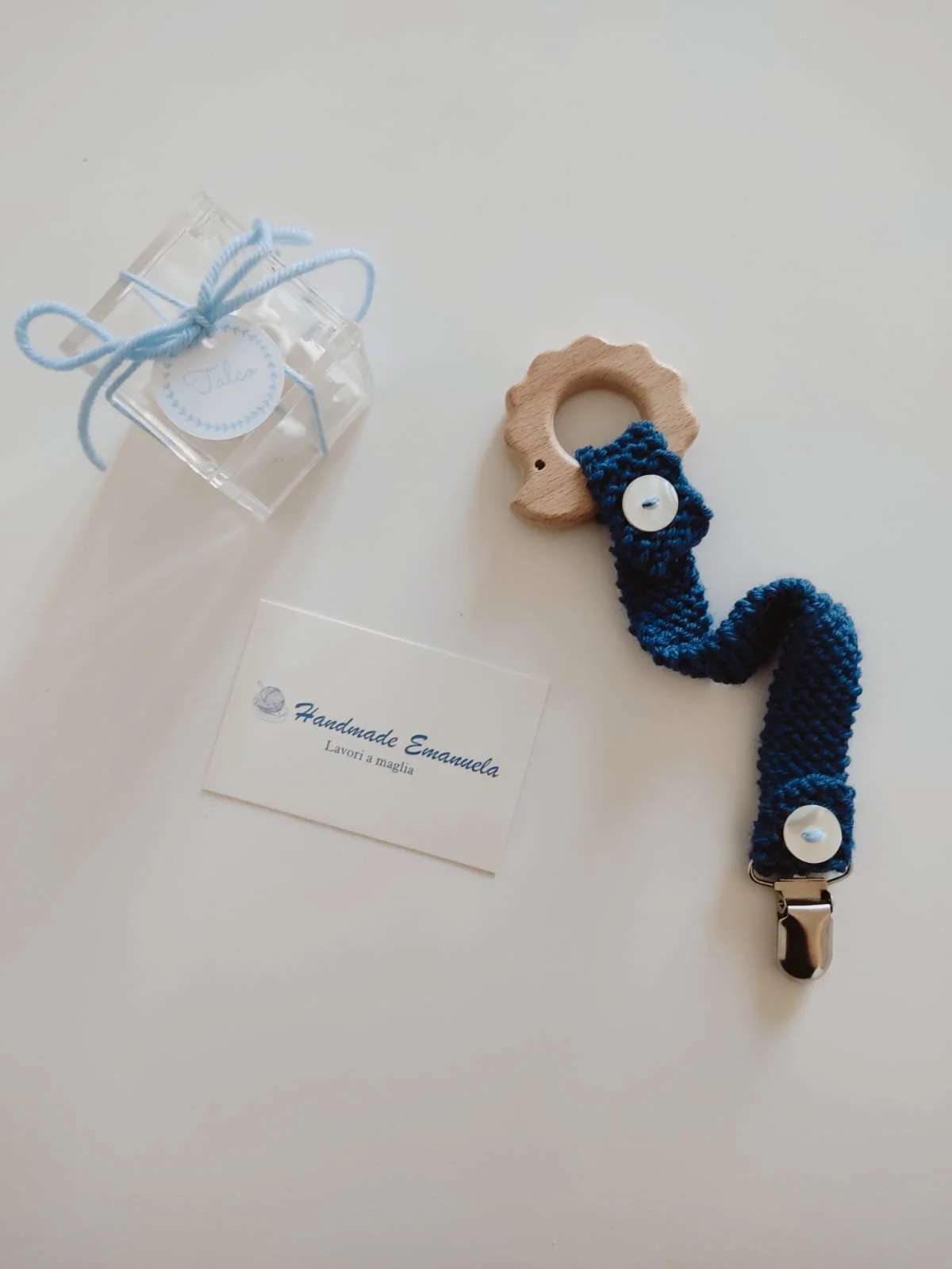 Portaciuccio in maglia blu scuro con giochino in legno a forma di riccio, due bottoni in madreperla e clip, con cartellino