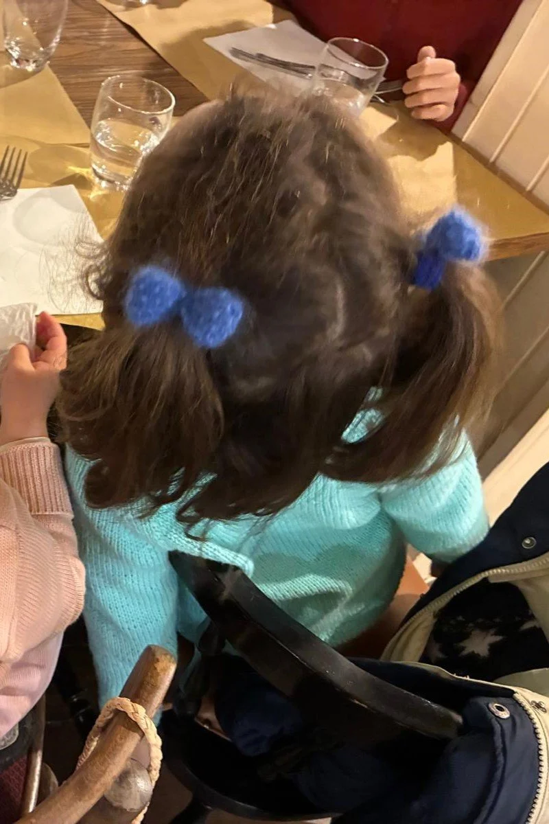 Dall’alto, bambina con capelli castani e due fiocchetti in mohair blu legati alle codine