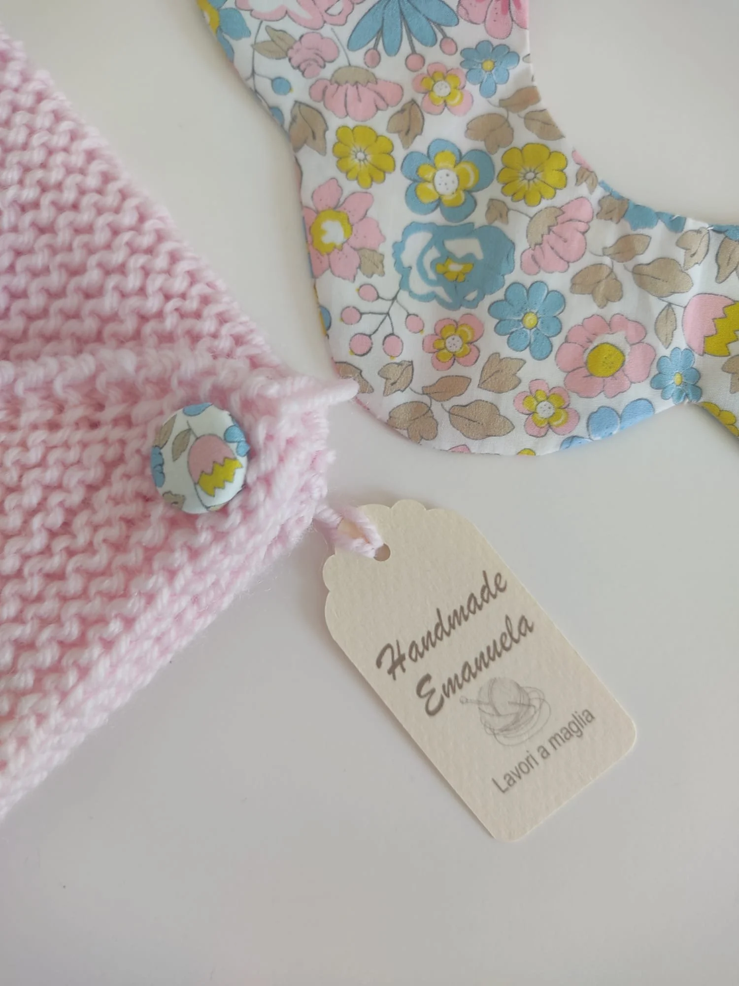 Dettaglio di un golfino rosa con bottone rivestito in tessuto floreale e cartellino appeso