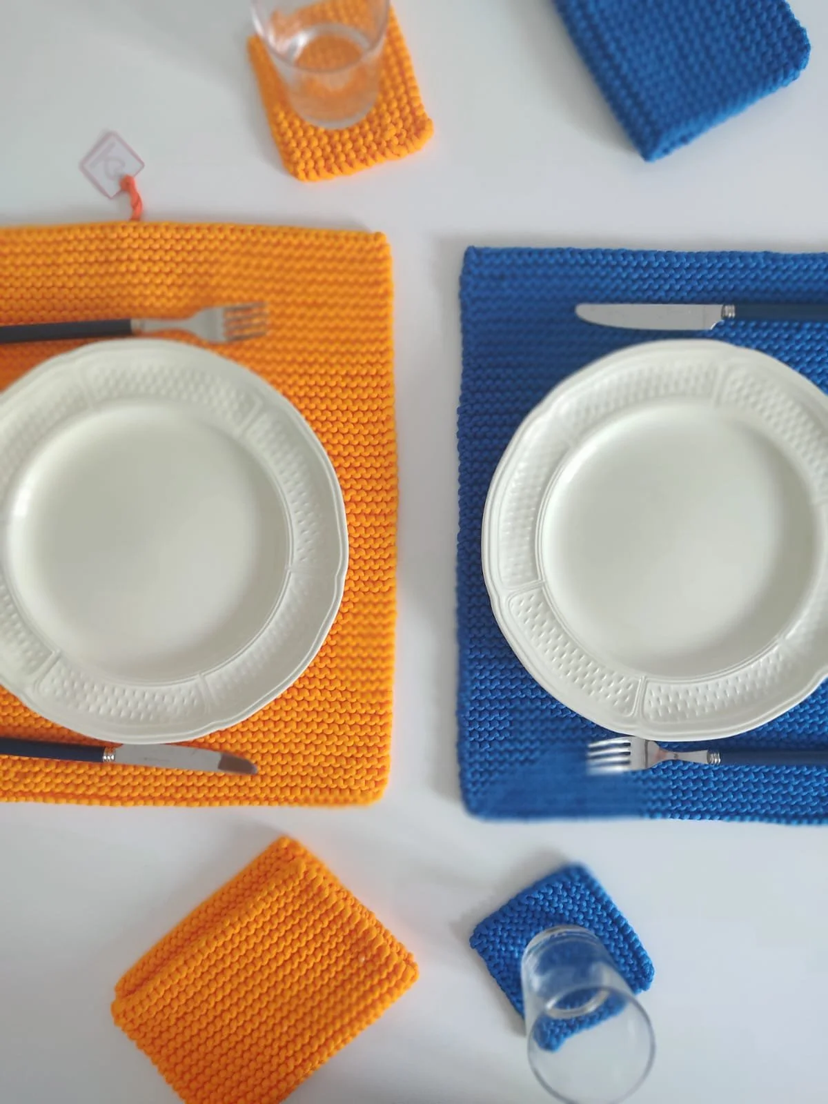 Tovagliette americane a maglia arancione e blu con sottobicchieri dello stesso colore, piatti bianchi e posate.