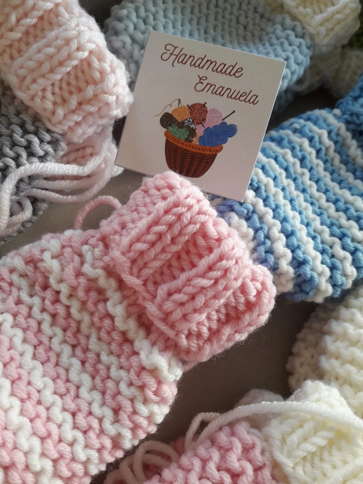 Moffole in maglia rosa, azzurre, crema e grigie, a tinta unita o a righine, impilate con un cartellino
