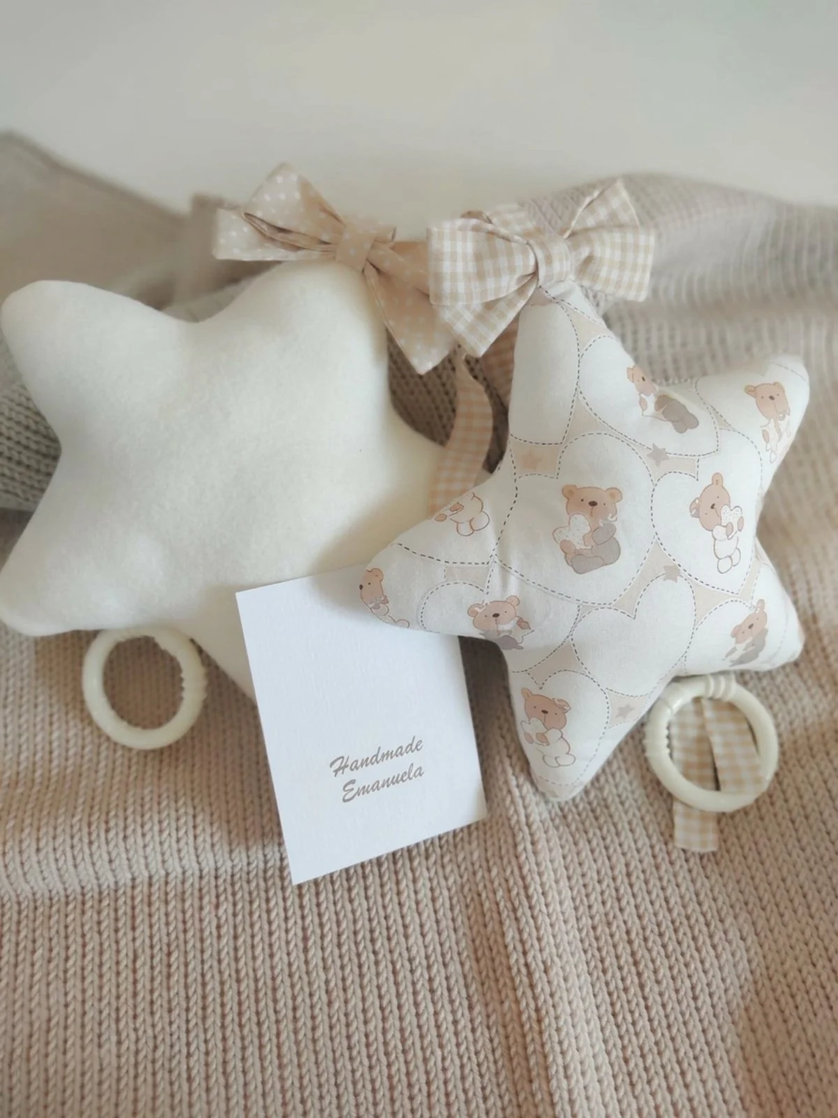 Due carillon a stella, uno panna e uno con orsetti e cuori beige, con fiocchi a pois e vichy su una coperta in maglia beige