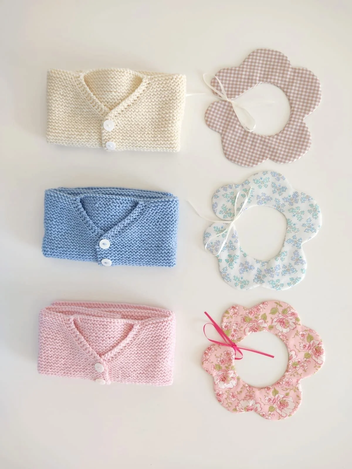 Tre golfini neonato piegati accanto a colletti a petalo in cotone vichy beige, fantasia azzurra e fiori rosa