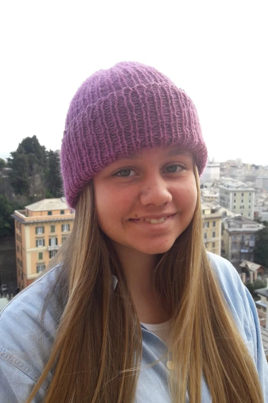 Ragazza sorridente con lunghi capelli castani che indossa un cappello in maglia lilla a coste con risvolto