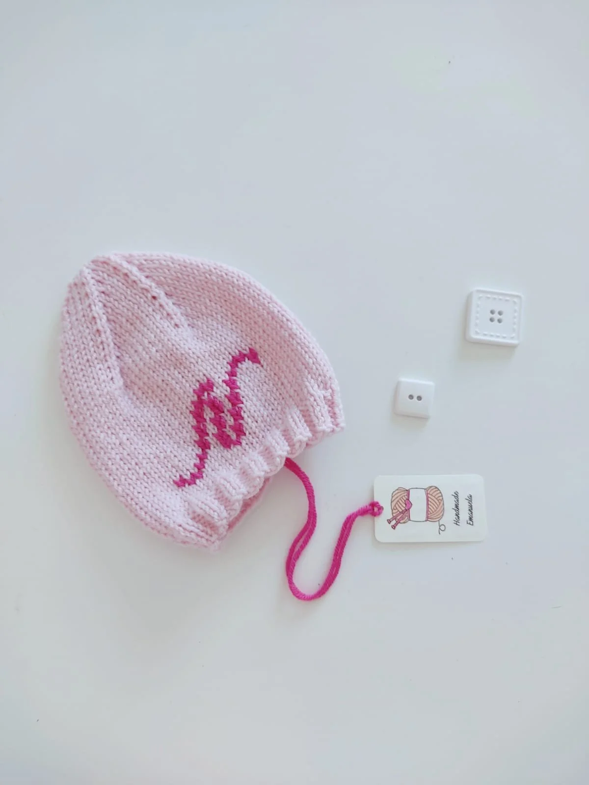 Cappellino in maglia rosa chiaro con iniziale ricamata fucsia e laccetto fucsia, con cartellino