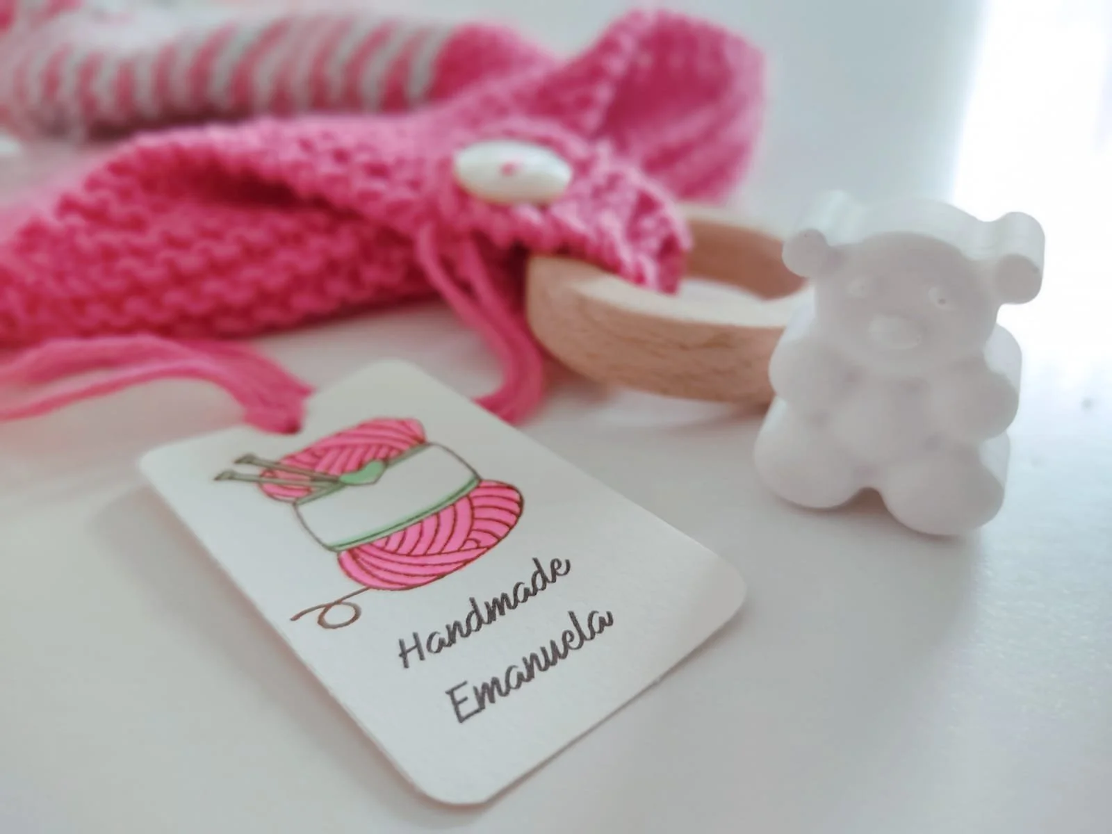 Primo piano di una linguetta in maglia fucsia con bottone, anello in legno e cartellino con logo