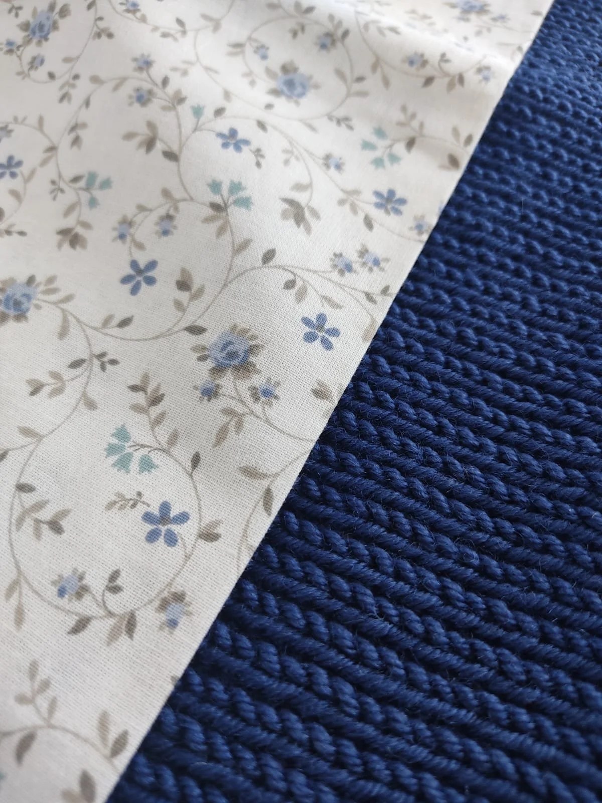 Dettaglio del cotone a fiorellini azzurri accanto a una coperta in maglia blu
