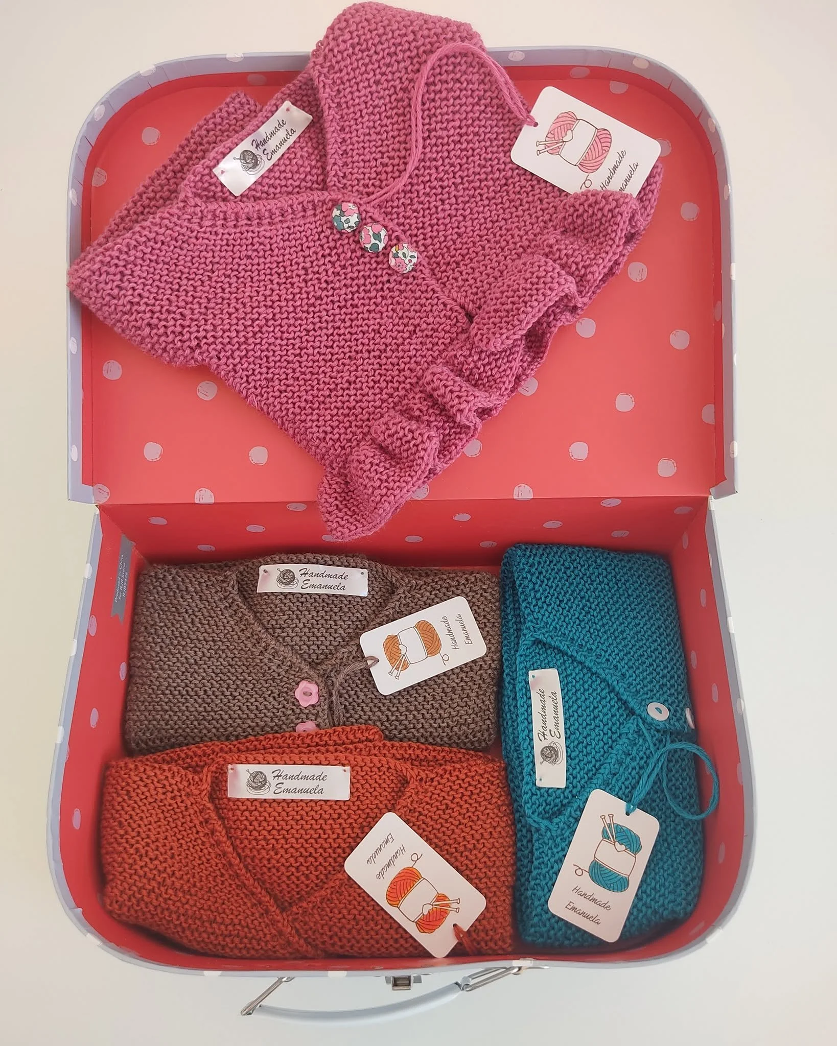 Valigetta a pois con quattro golfini a maglia in rosa, marrone, ruggine e petrolio, con etichette Handmade Emanuela.