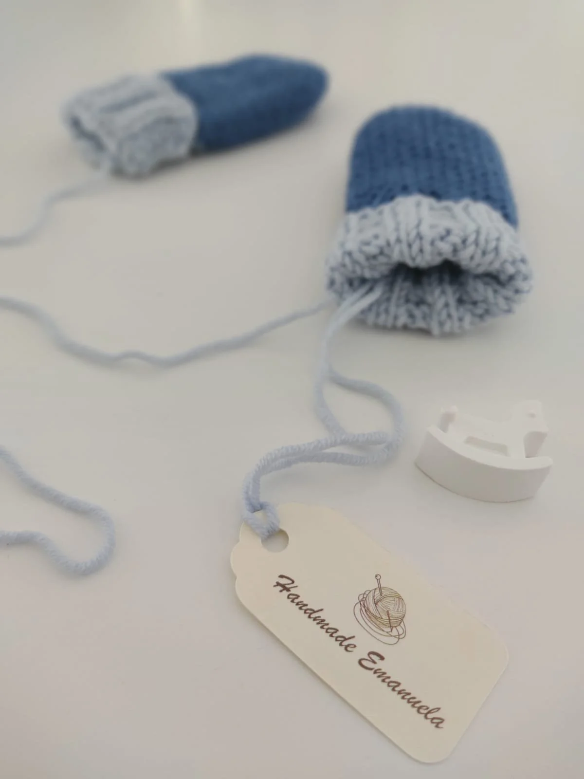Primo piano di moffole in maglia blu con polsino azzurro e laccetto, con cartellino in primo piano