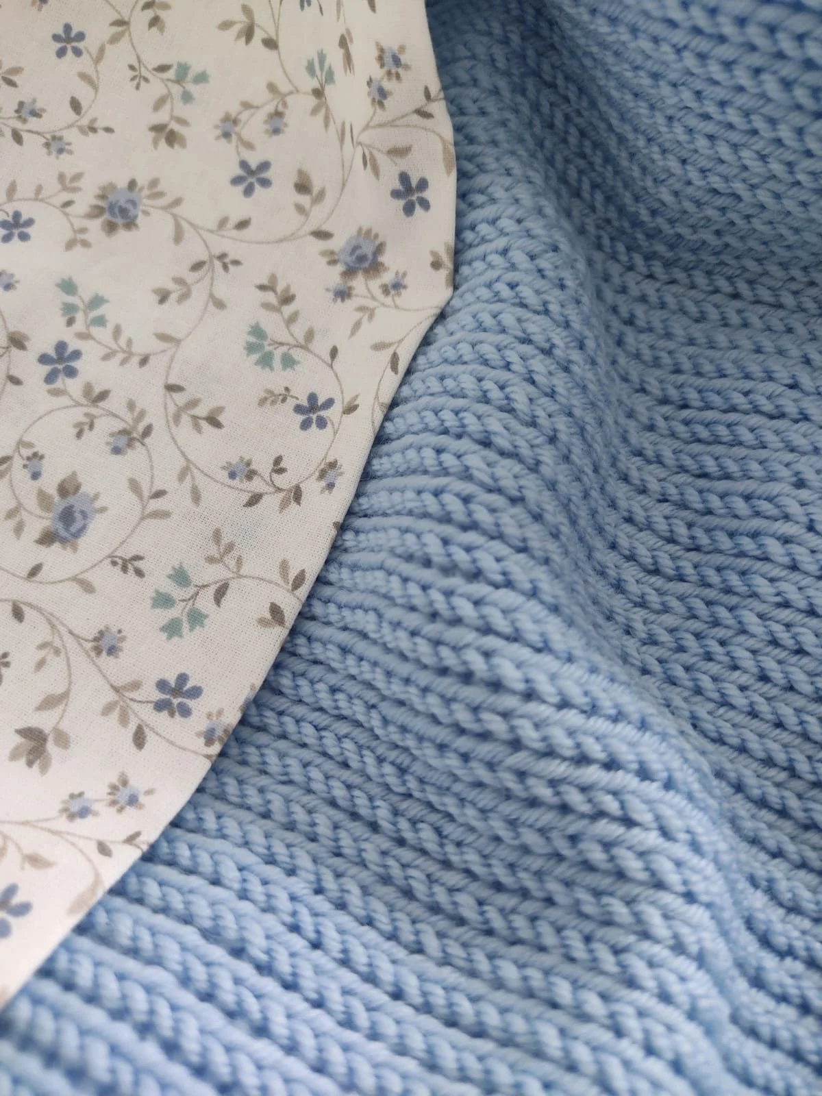 Dettaglio del cotone a fiorellini azzurri accanto a una coperta in maglia azzurra