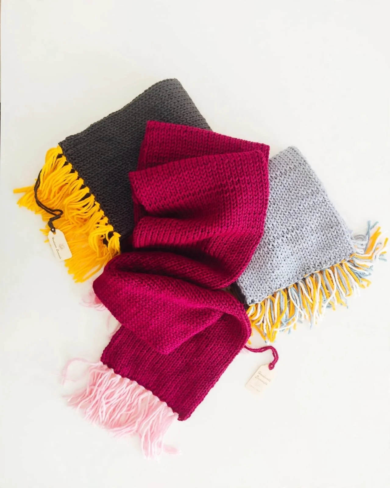 Tre sciarpe in maglia fucsia, antracite e grigio chiaro, con frange rosa, gialle e multicolore