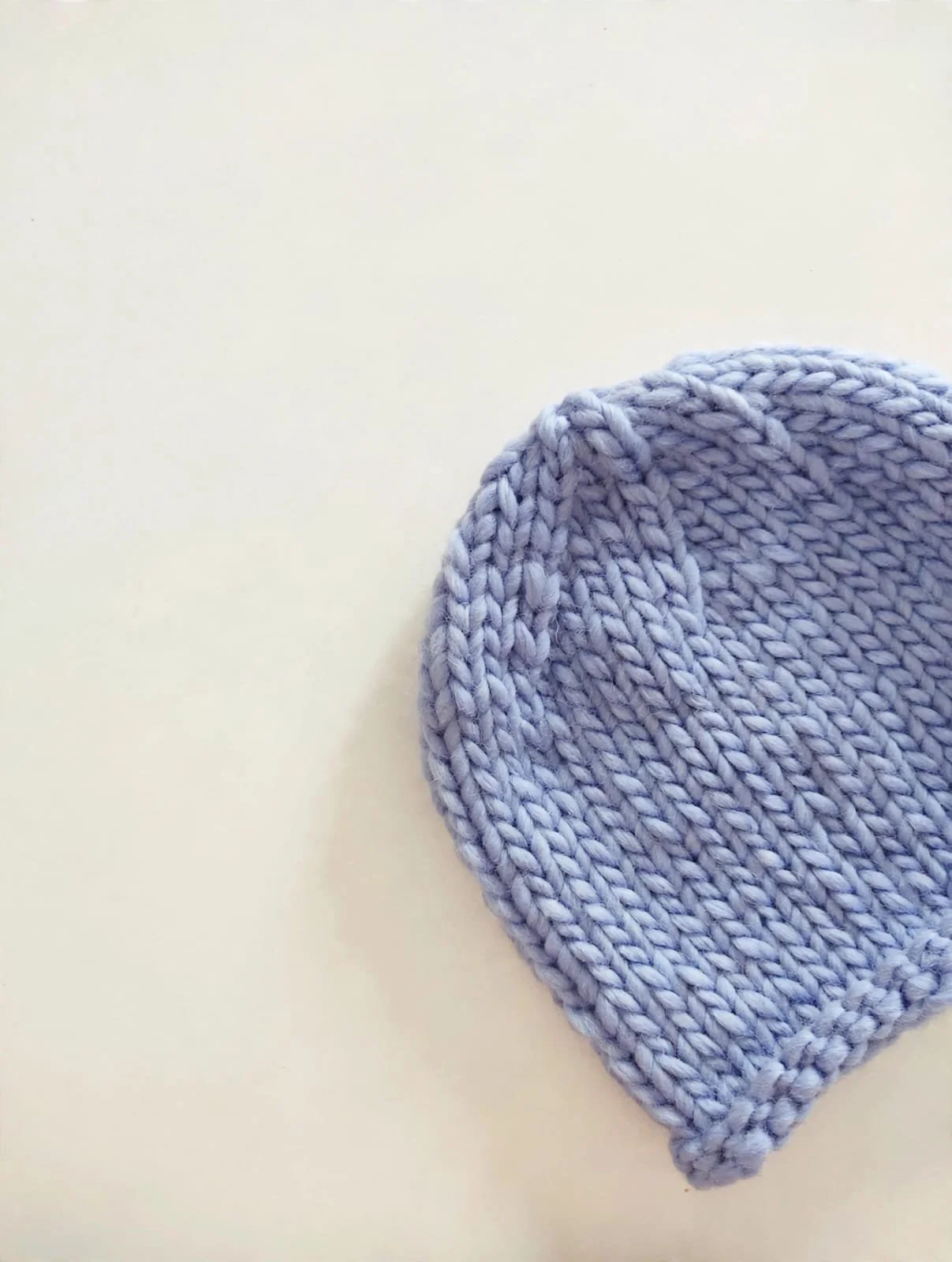 Cappello in lana grossa color lavanda a maglia larga, appoggiato su fondo crema