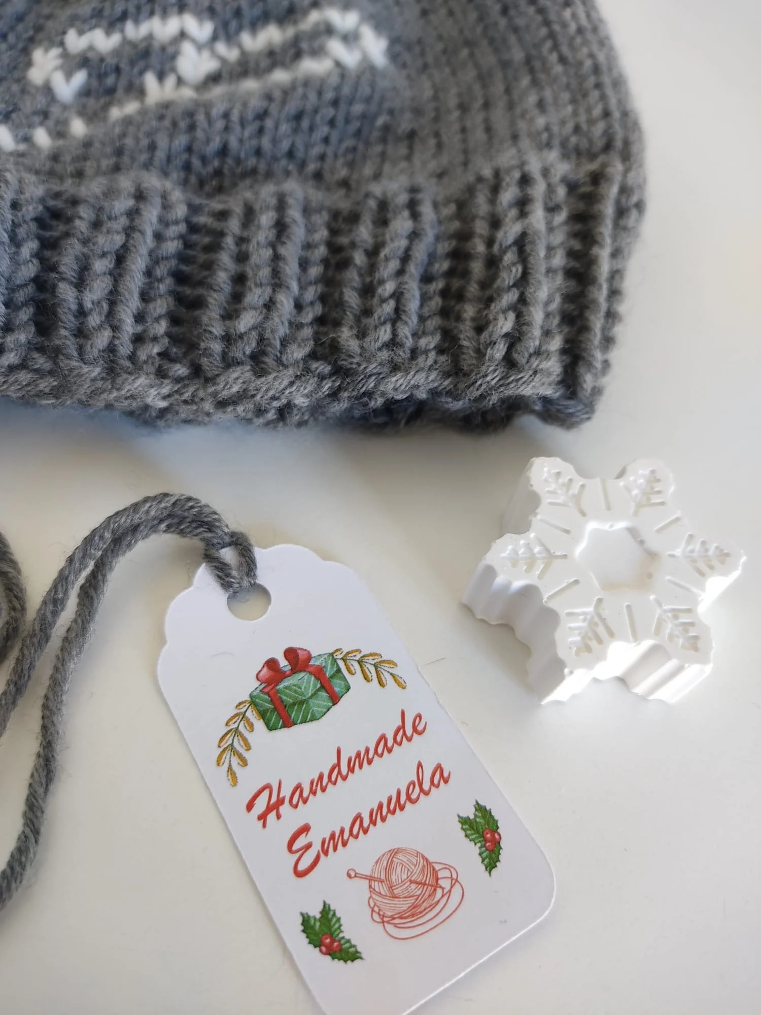 Gessetto bianco a forma di fiocco di neve accanto a un cappellino in maglia grigio e a un cartellino natalizio