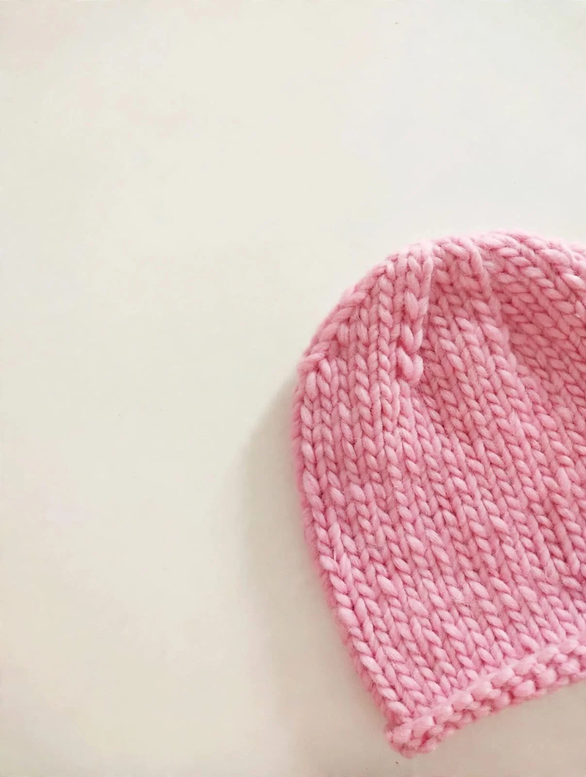 Cappello in lana grossa rosa chiaro a maglia larga, appoggiato su fondo crema