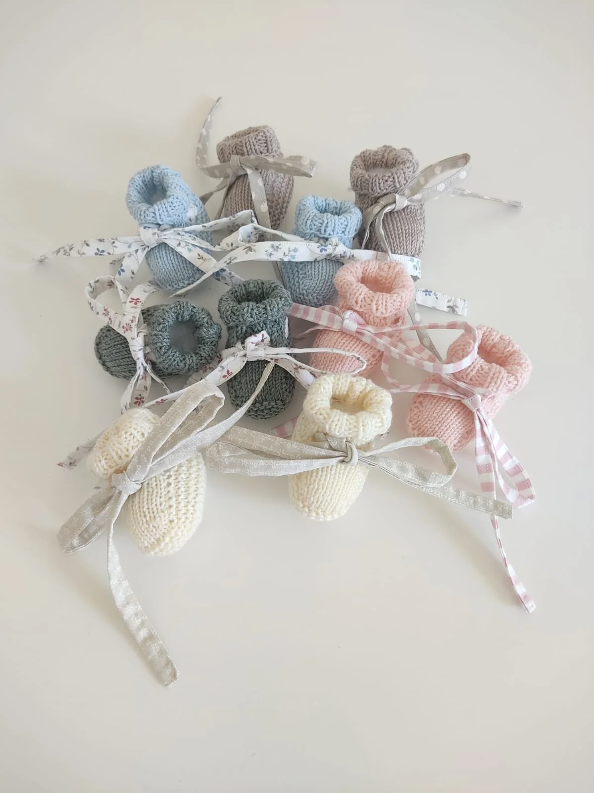 Cinque paia di scarpine a maglia in azzurro, tortora, verde, rosa e panna, con nastrini in stoffa a fantasia.