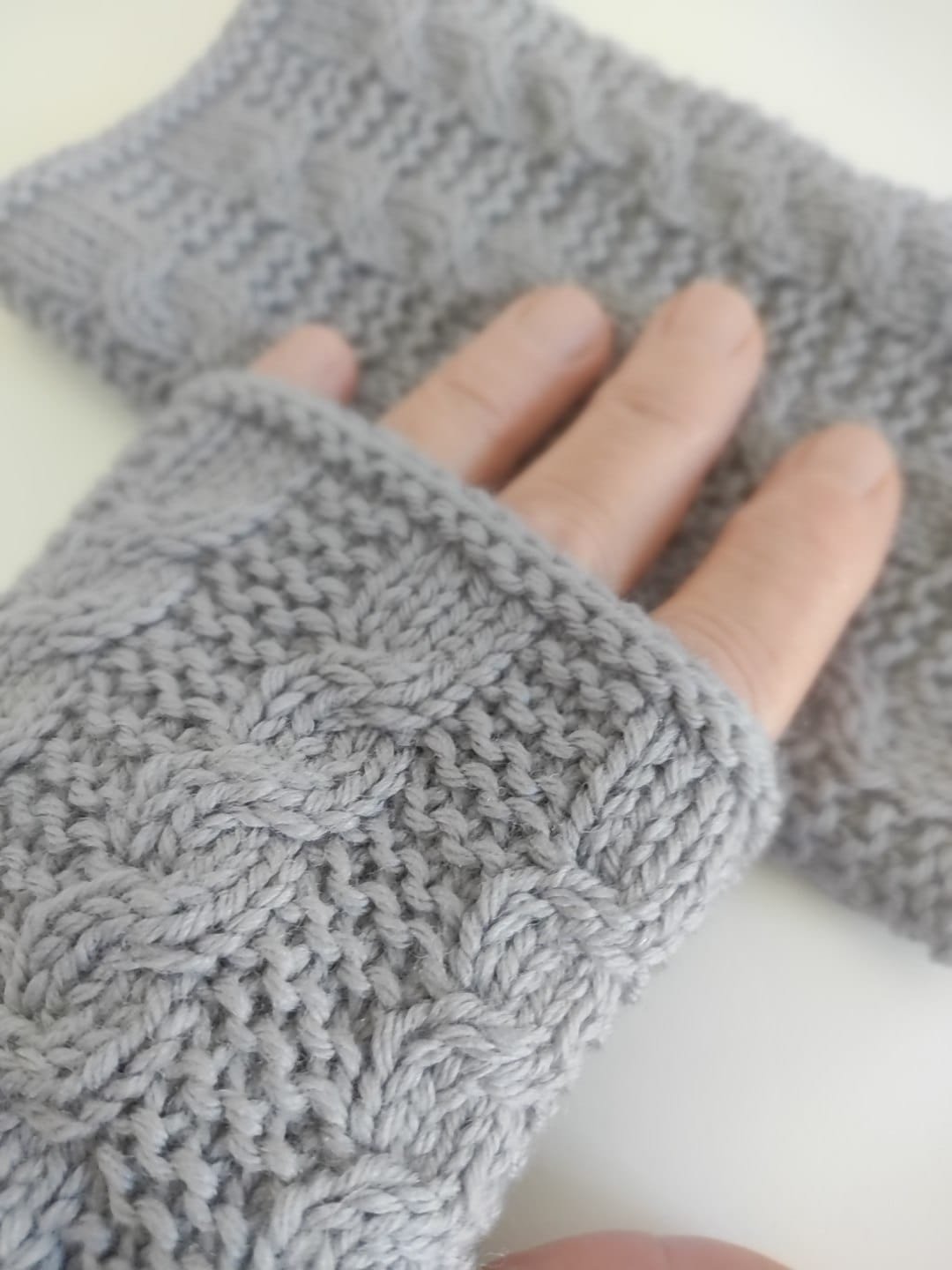 Primo piano di un guantino senza dita in maglia grigia a trecce, con le dita libere