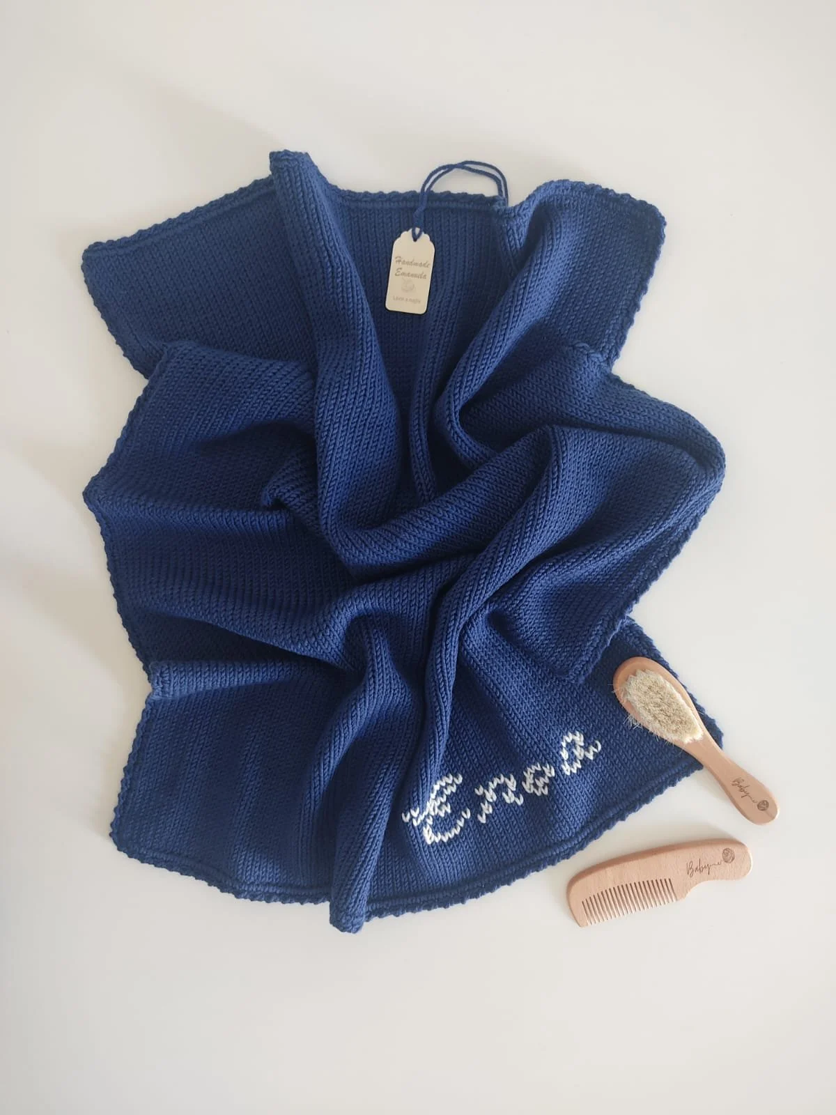 Copertina a maglia blu con un nome lavorato in bianco e cartoncino Handmade Emanuela.