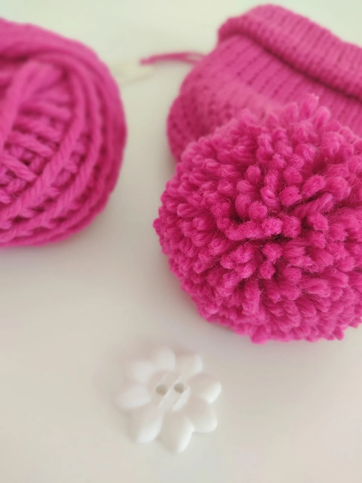 Primo piano di un pompon fucsia su un cappello in maglia, accanto a un gomitolo fucsia