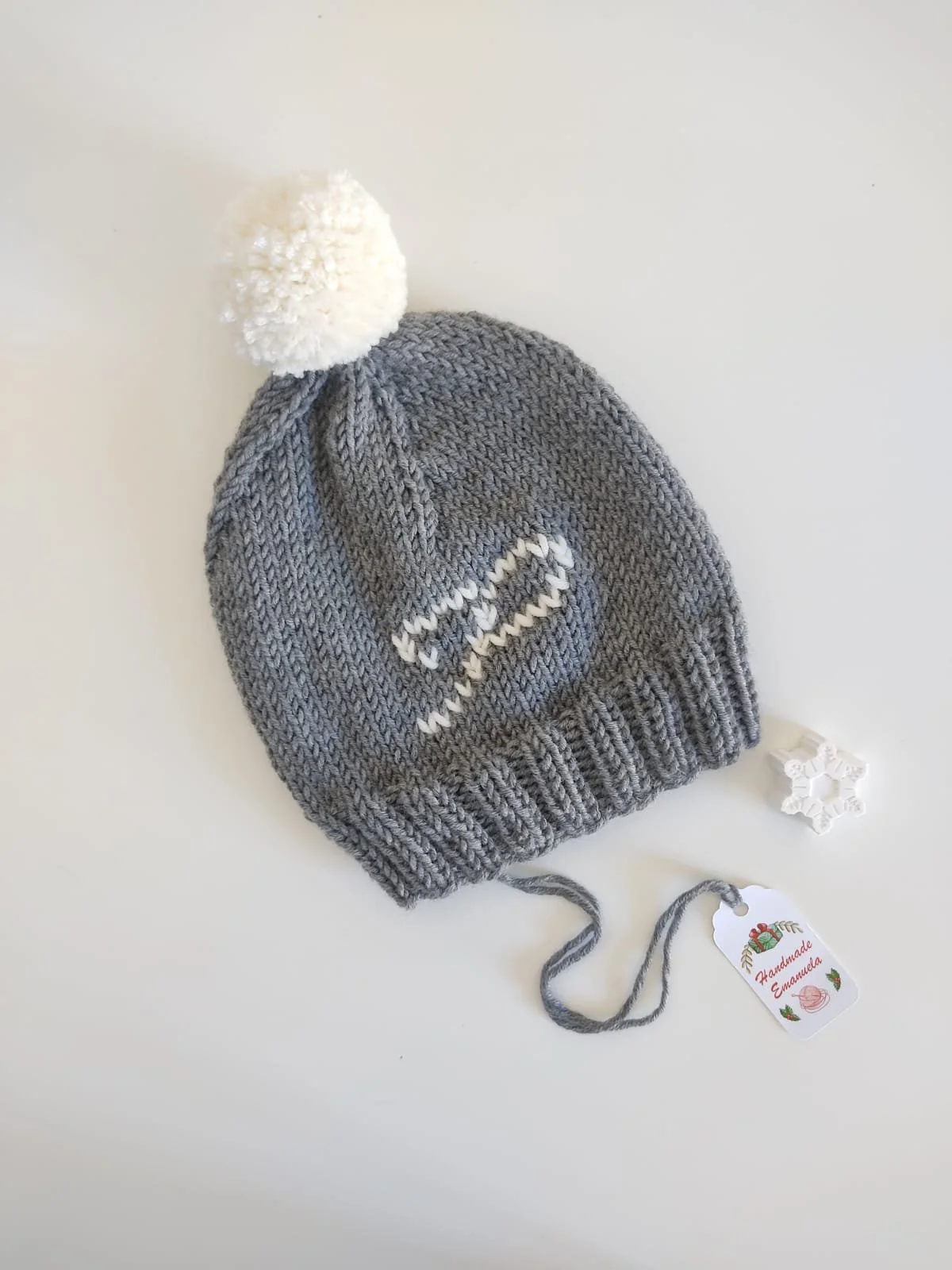 Cappello in maglia grigio con pompon crema, iniziale ricamata crema e bordo a coste, con cartellino