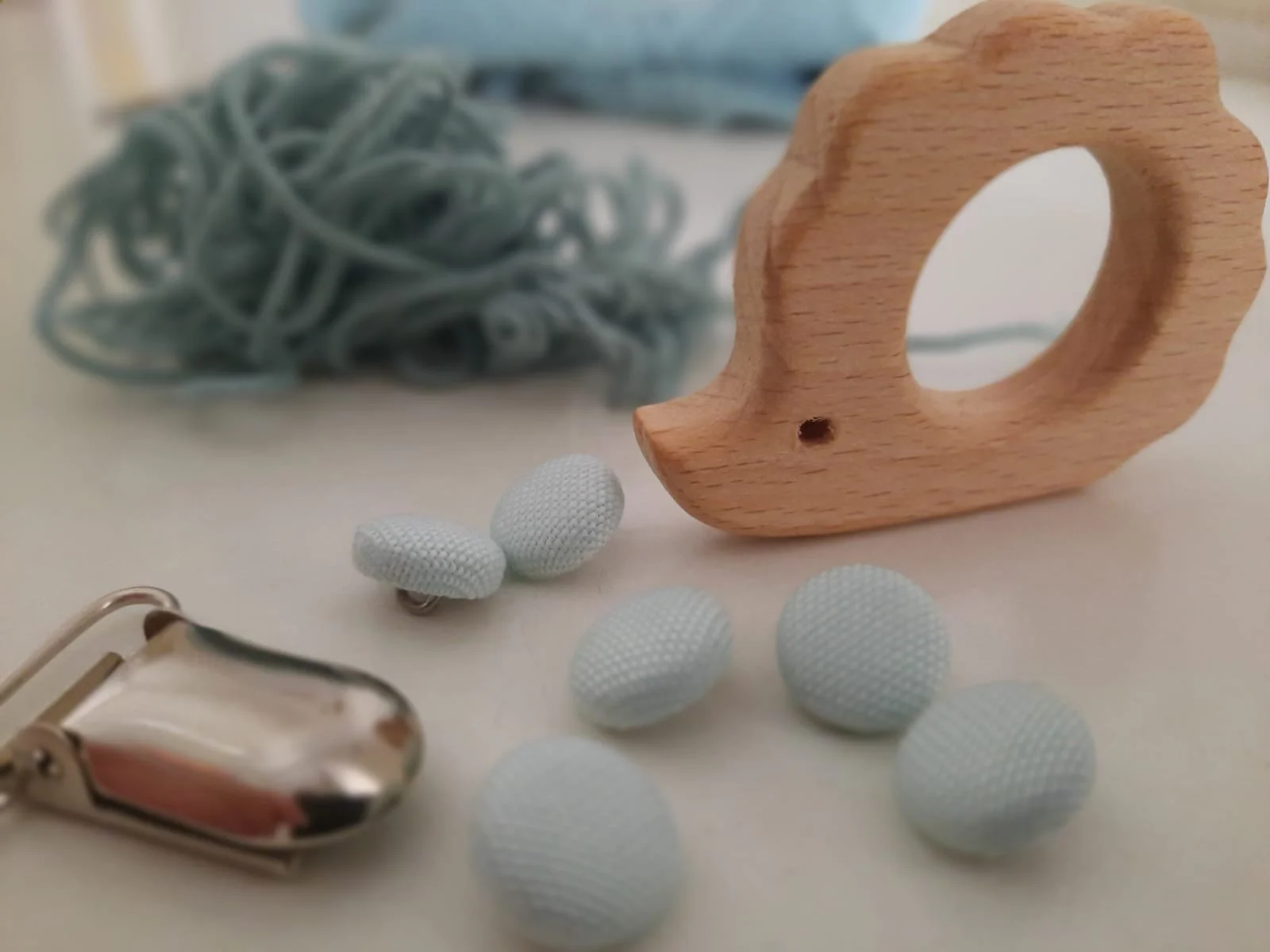 Primo piano di bottoni rivestiti in tessuto azzurro chiaro, giochino in legno a forma di riccio e clip in metallo