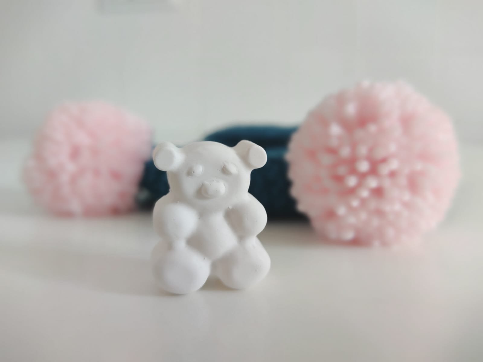Gessetto bianco a forma di orsetto in primo piano, con due pompon rosa sfocati sullo sfondo