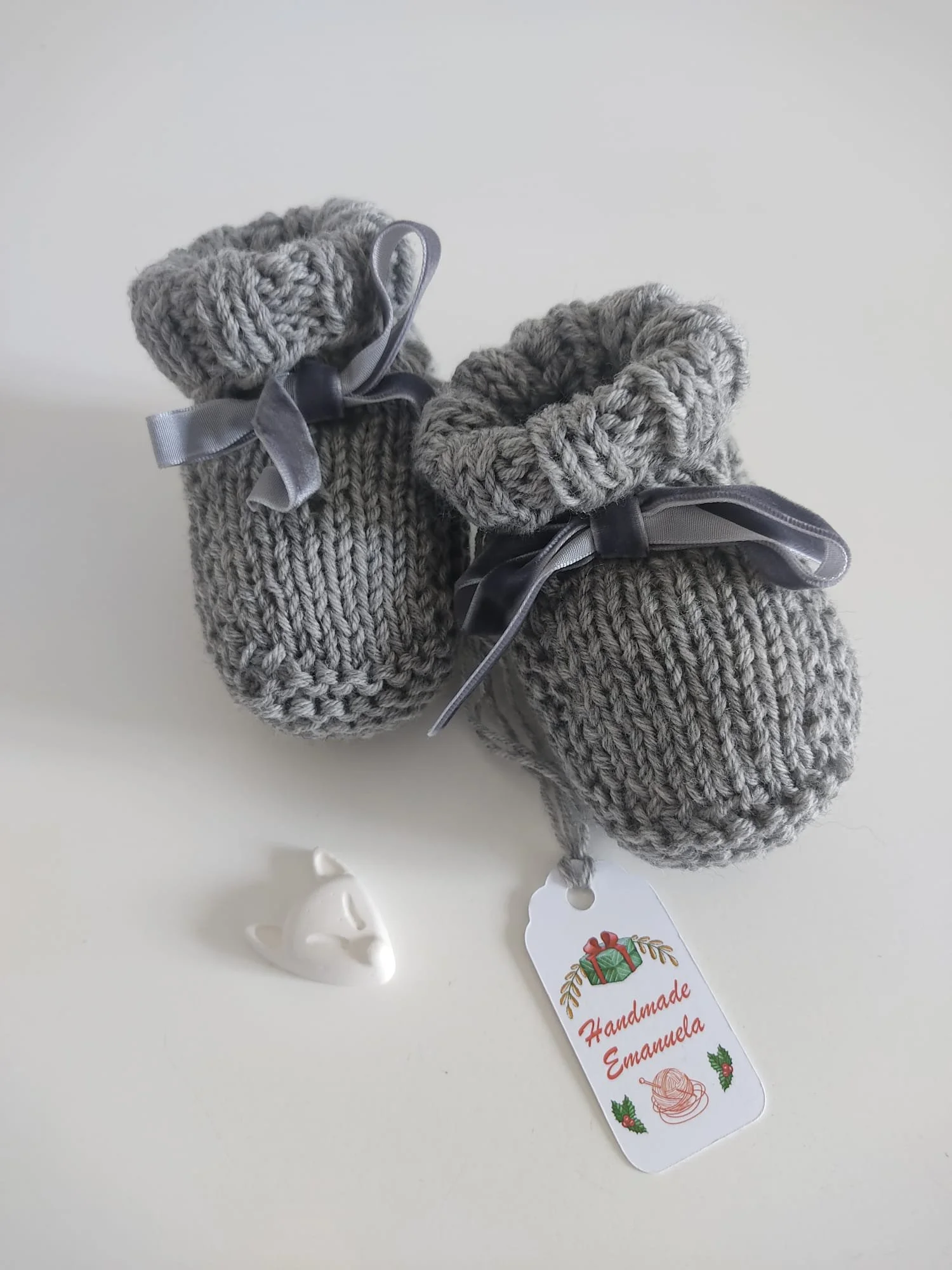 Scarpine a maglia grigie con nastrino in velluto grigio annodato a fiocco, su fondo bianco.