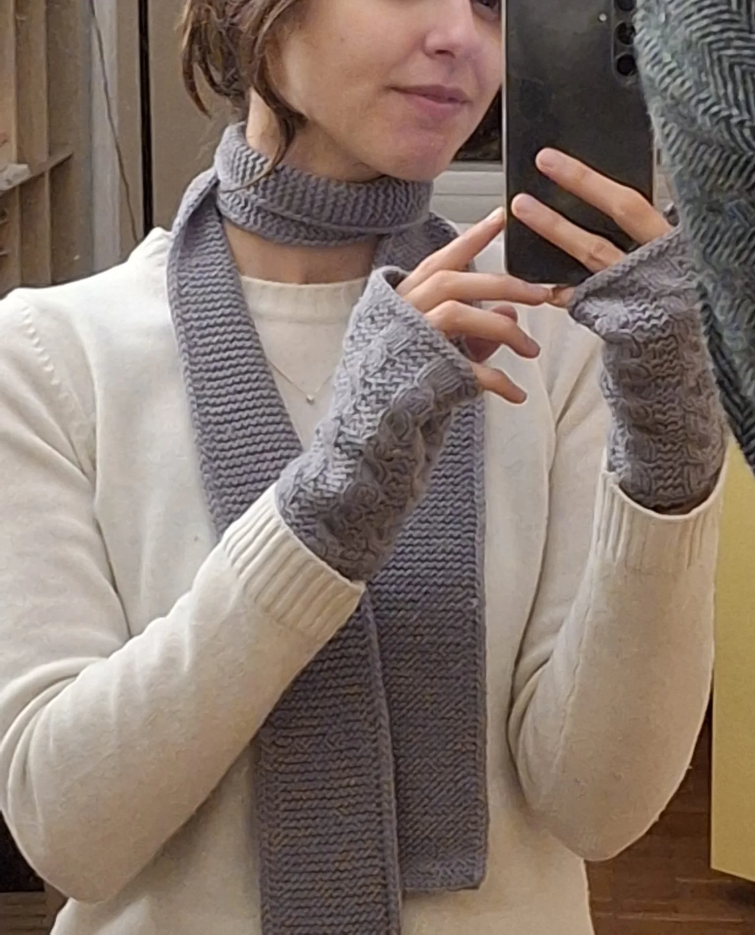 Donna con sciarpa sottile in maglia grigia al collo e manicotti coordinati, maglione panna