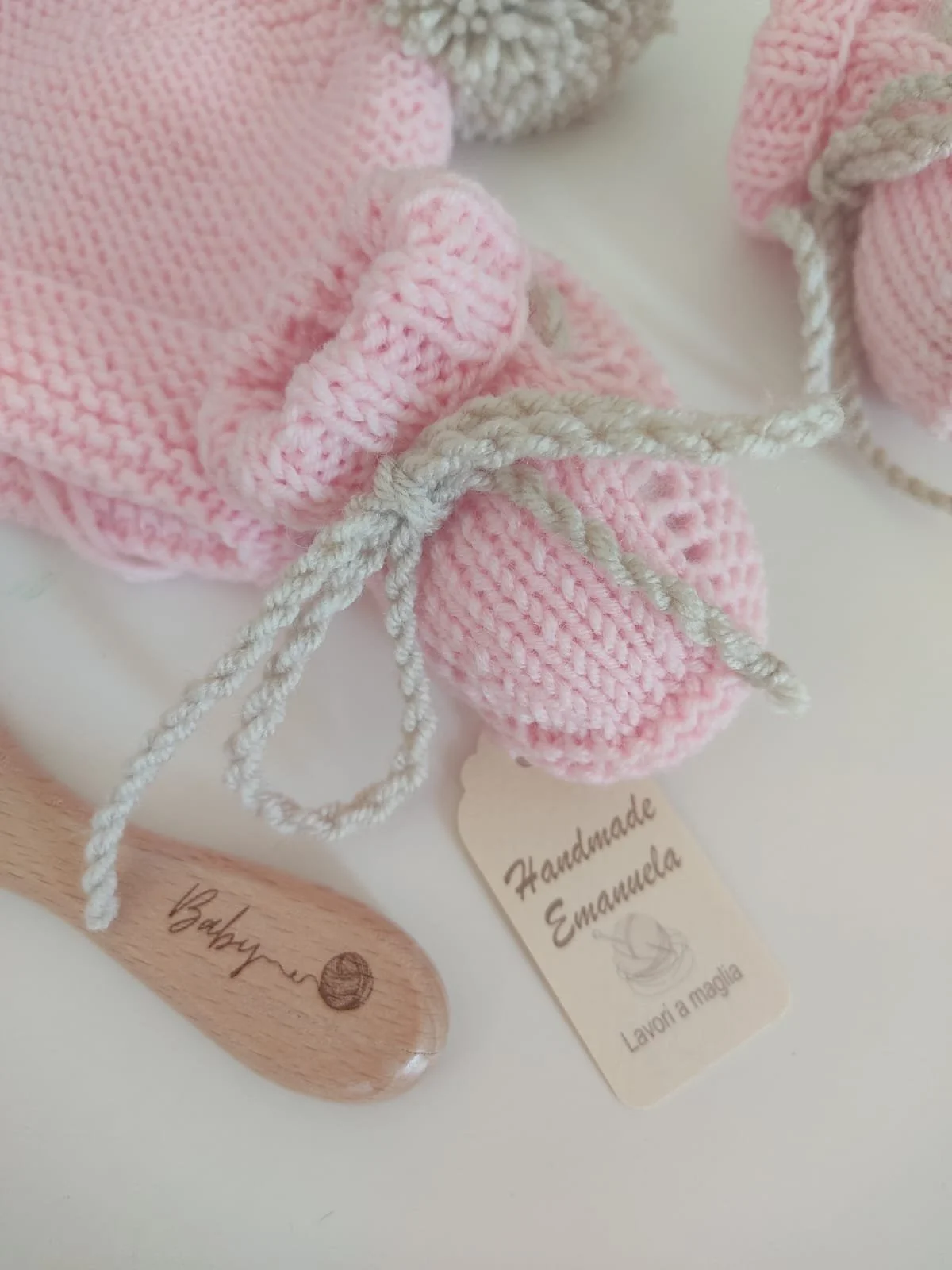 Dettaglio di scarpine in maglia rosa con laccio beige, cartellino e spazzolina in legno con incisione Baby