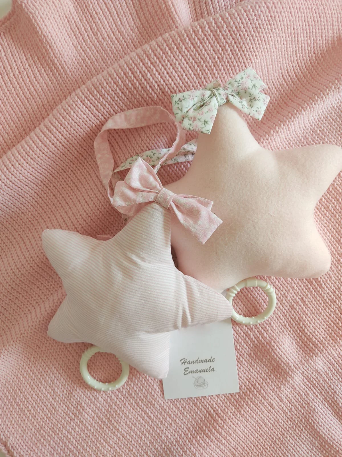 Due carillon a stella rosa, uno a righe e uno in tinta unita, con fiocchi floreali su una coperta in maglia rosa