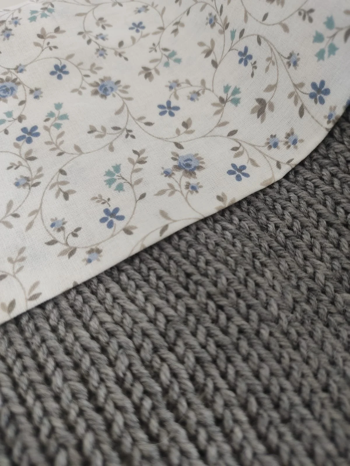 Dettaglio del cotone a fiorellini azzurri accanto a una coperta in maglia grigia