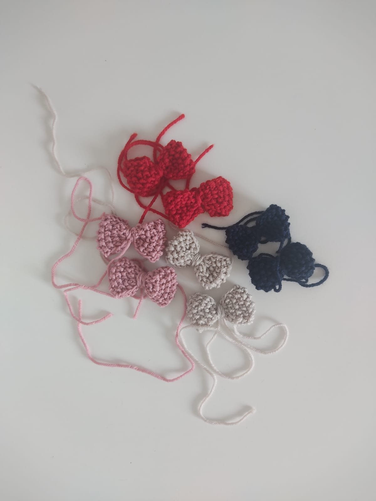 Fiocchetti in lana lavorati a maglia a punto riso in rosso, rosa, beige e blu su sfondo bianco