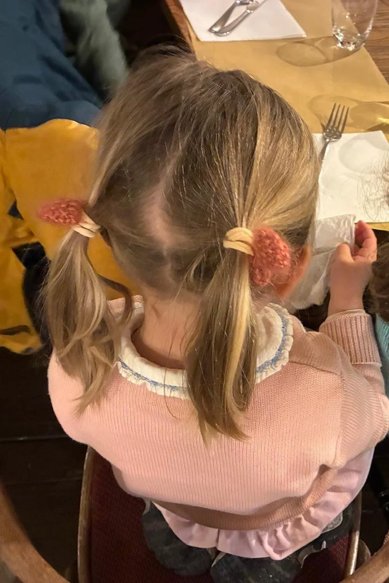 Dall’alto, bambina con due codine bionde fermate da fiocchetti in lana corallo
