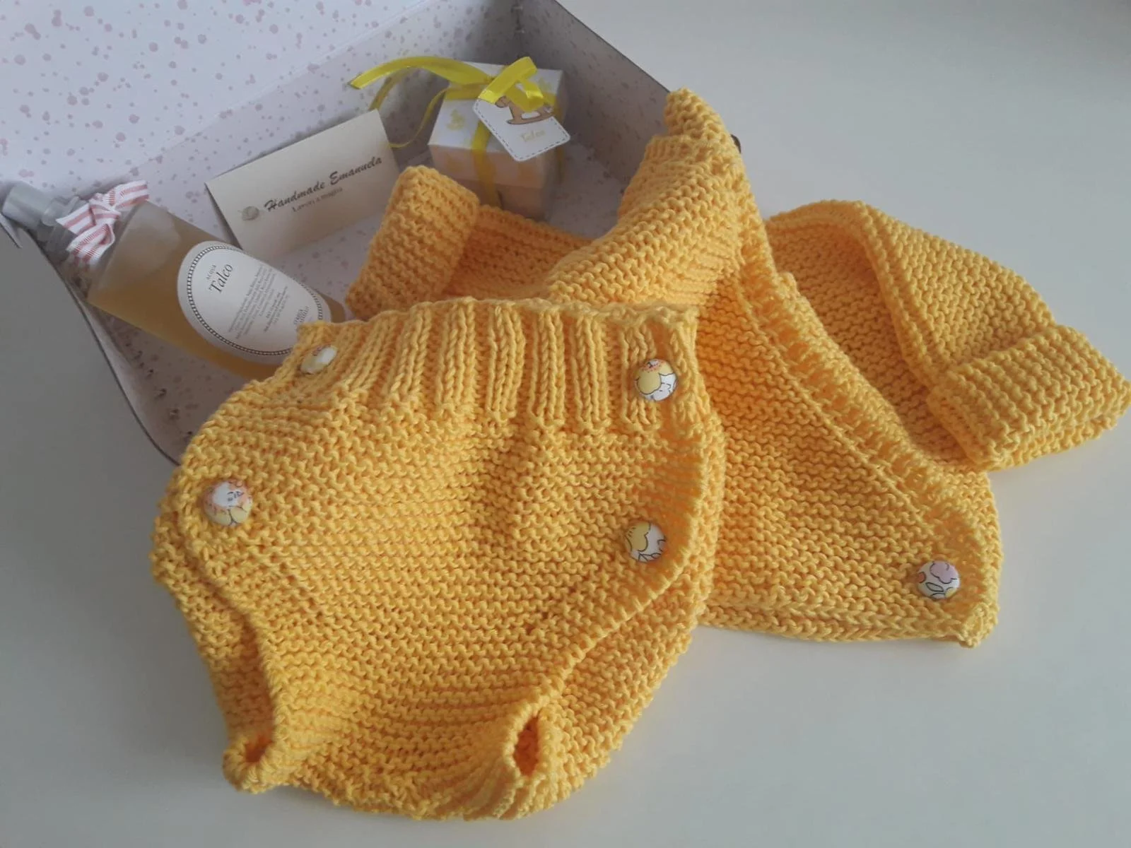 Culotte a maglia gialla con bottoni in stoffa a fiori, con un capo giallo coordinato, in una scatola con acqua al talco.