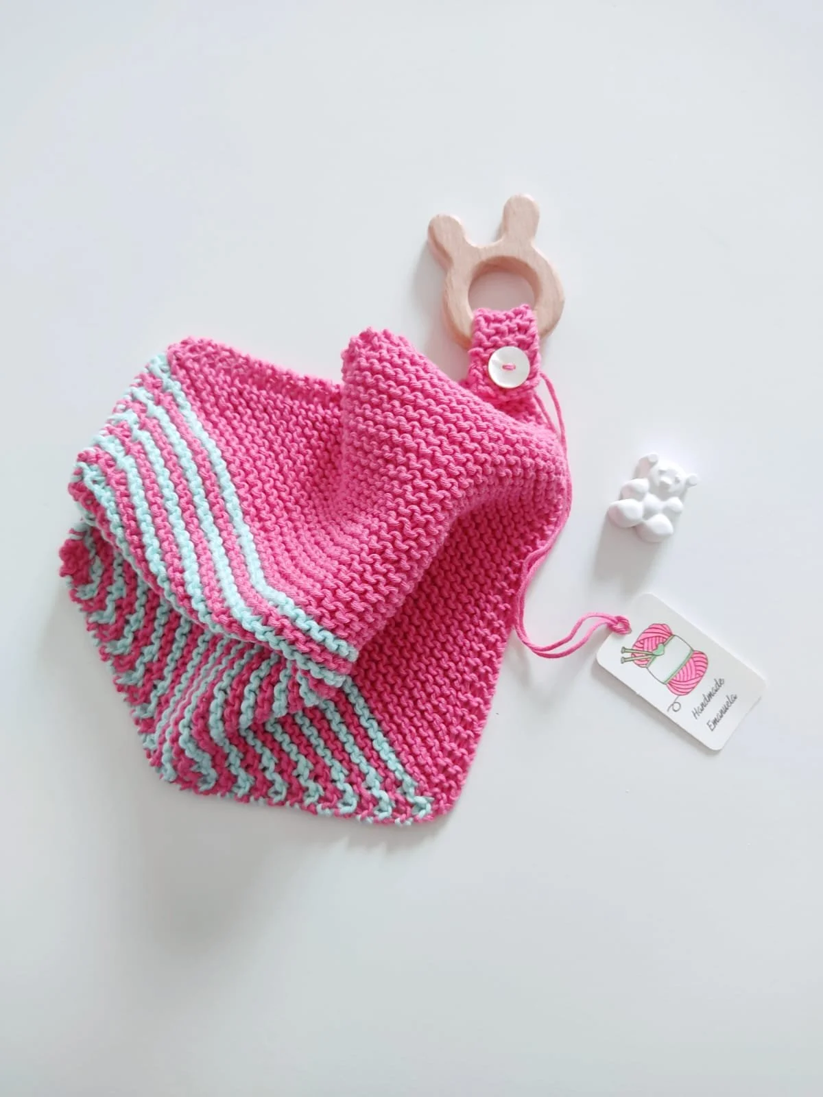 Doudou in maglia fucsia con righe verde acqua e giochino in legno a forma di coniglietto, con cartellino