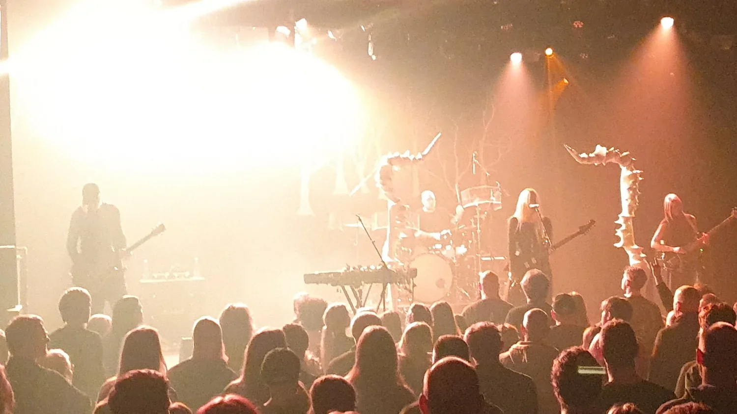 Band performing on stage in front of an audience, with bright lights and smoke effects.