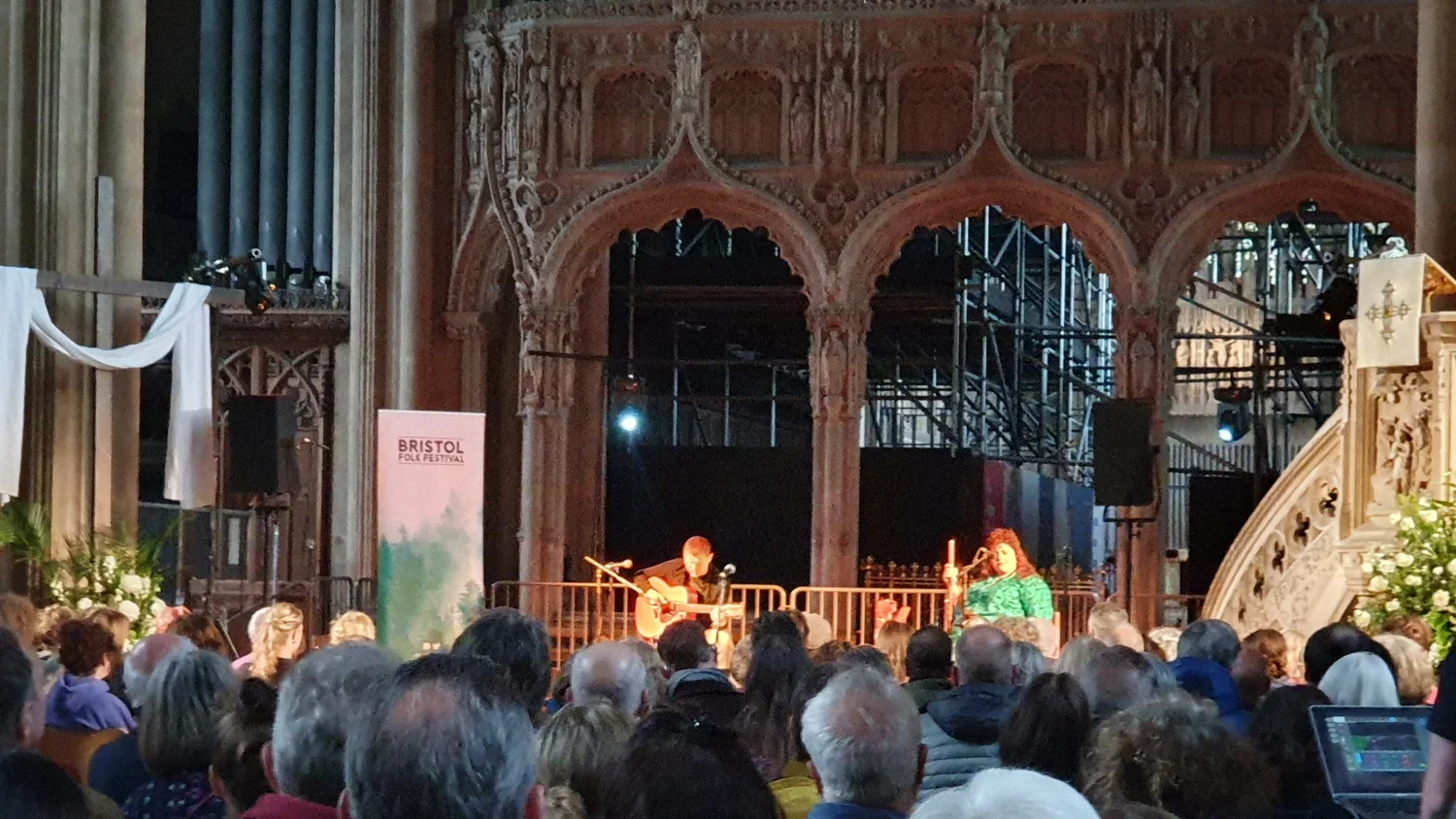 A live music performance at the Bristol Folk Festival inside a historic venue with ornate architectural details and a large audience.